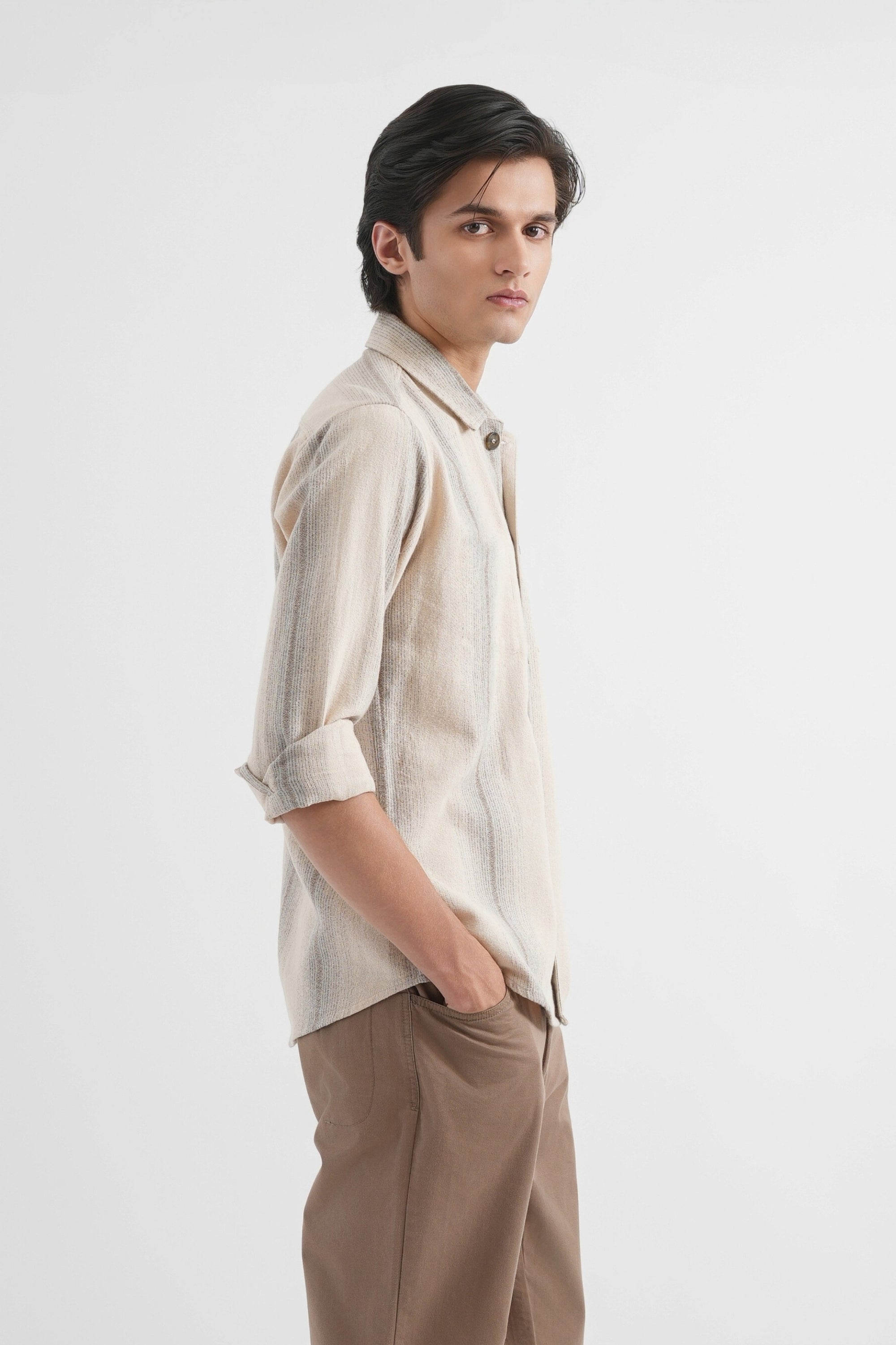 Man wearing a beige shirt and brown pants on a white background
