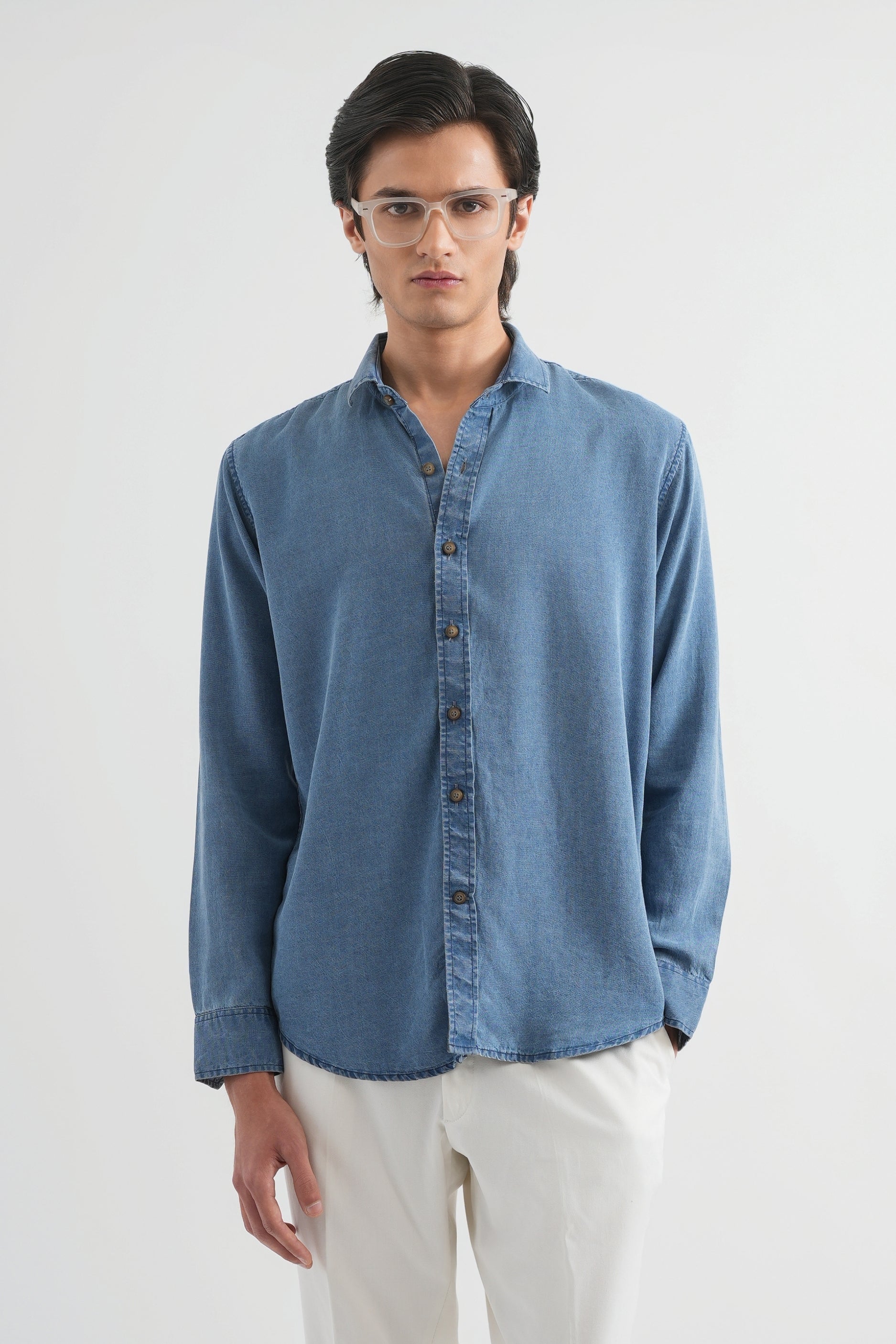 Man wearing a blue denim shirt and white pants on a plain background