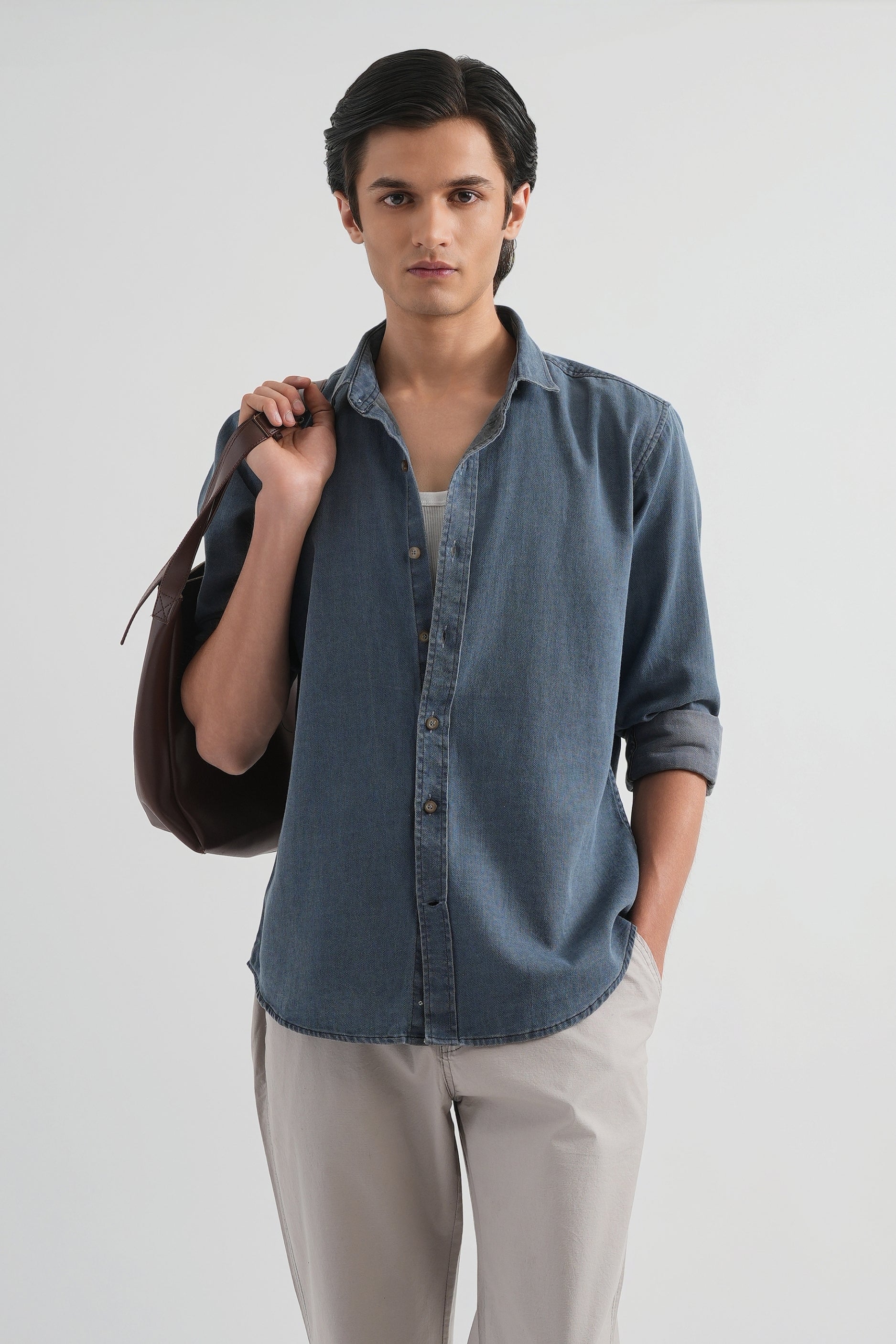 Man wearing a blue shirt and beige pants holding a black bag on a white background