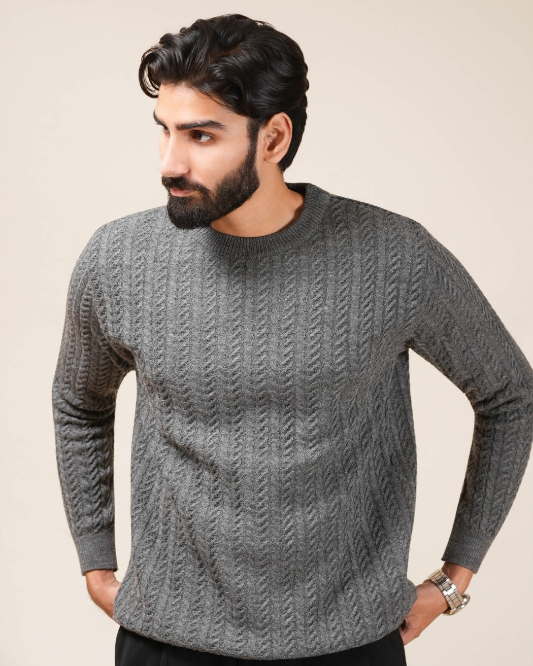 Man wearing a gray cable knit sweater against a plain background