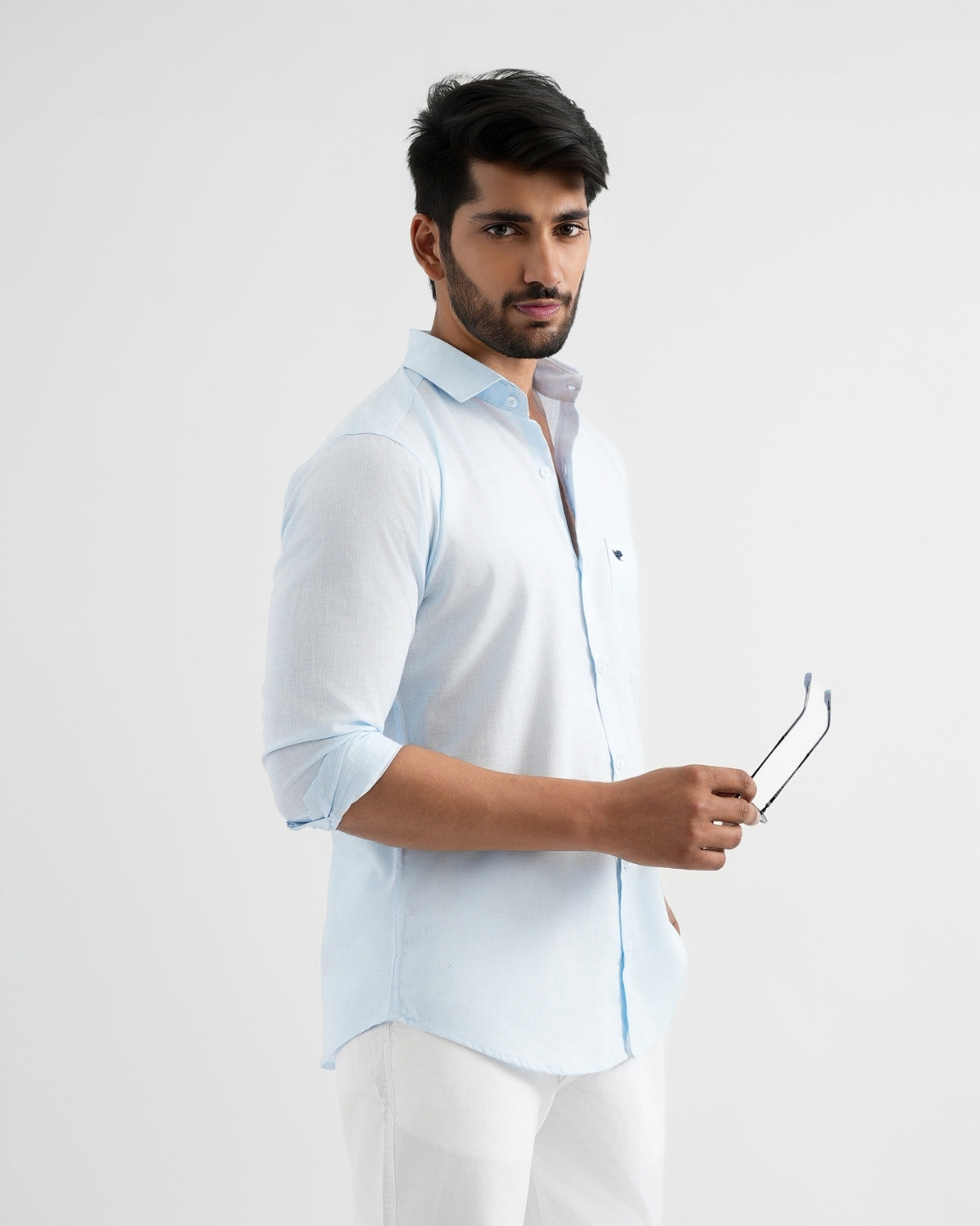 Man wearing a light blue shirt with rolled-up sleeves against a white background