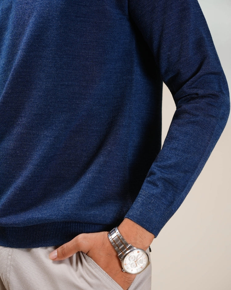 Person wearing a blue sweater with a silver watch on a neutral background