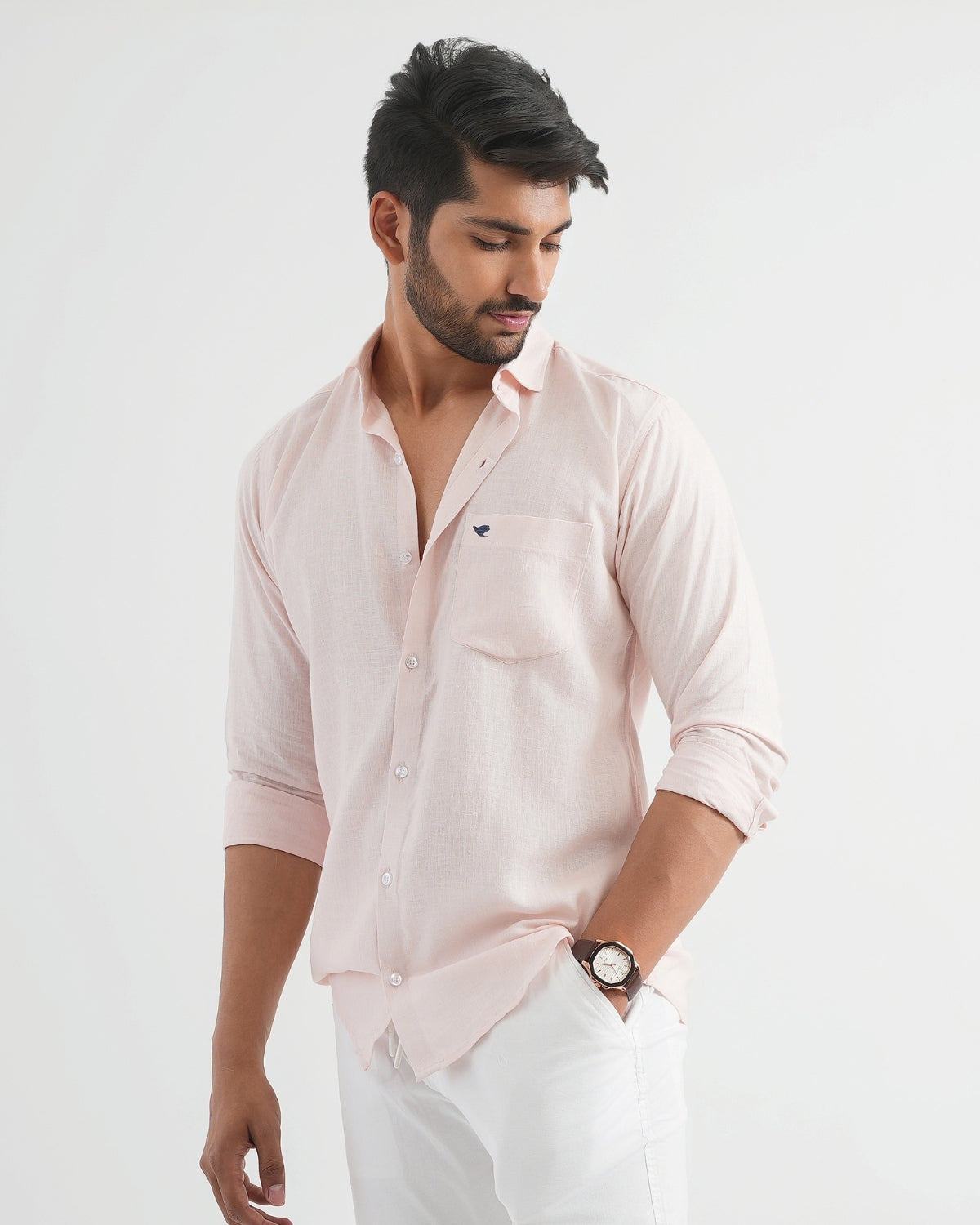Man wearing a light pink shirt with a small logo on a white background