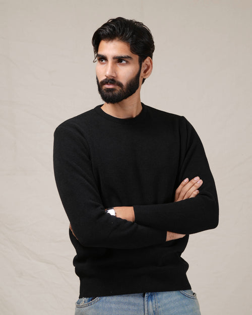 Man wearing a black sweater with arms crossed against a neutral background