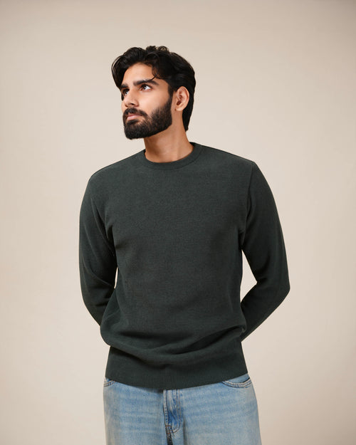 Man wearing a dark green sweater and light blue jeans against a beige background
