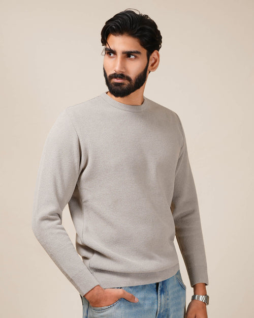 Man wearing a gray sweater and blue jeans against a beige background