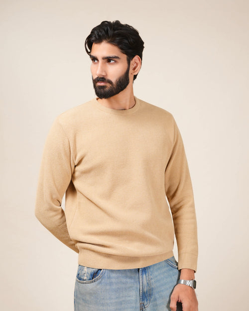 Man wearing a beige sweater and blue jeans against a plain background