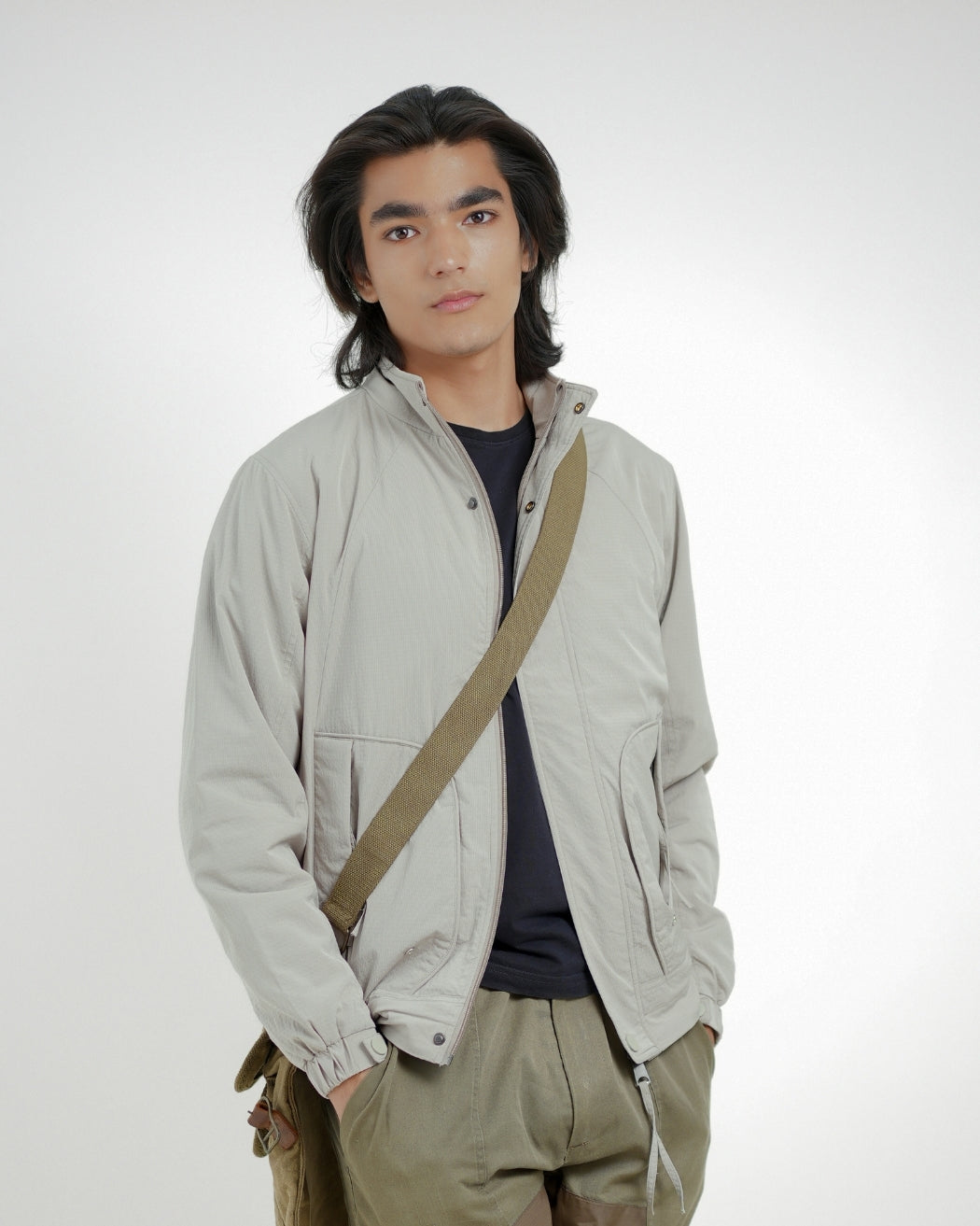 Man wearing a light gray jacket with a brown strap over his shoulder on a white background