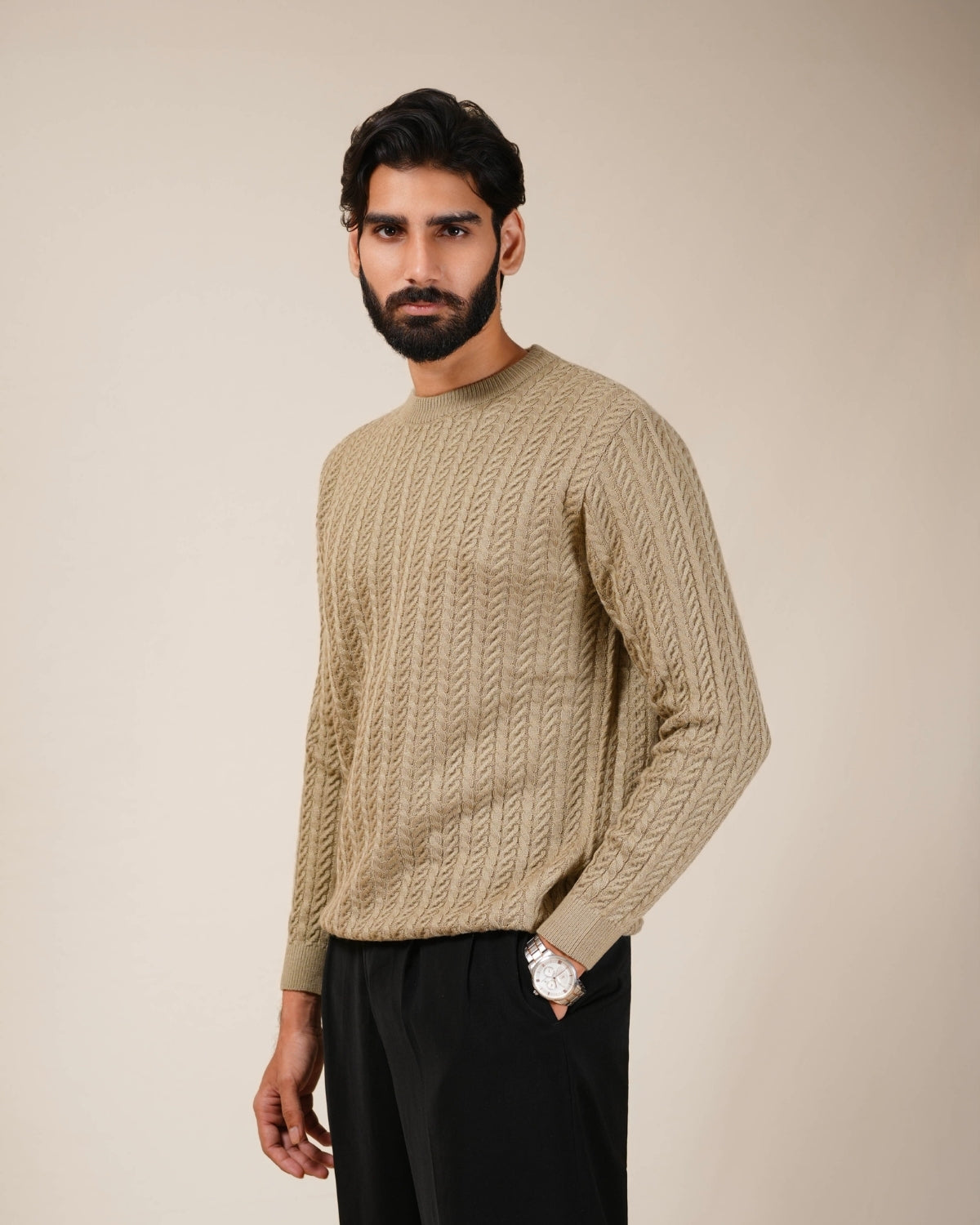 Man wearing a beige cable knit sweater against a beige background
