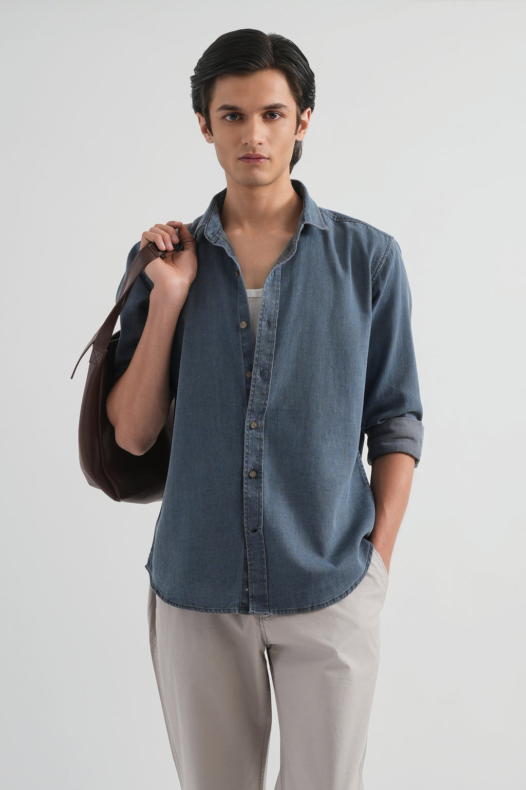 Man wearing a blue shirt and beige pants holding a black bag on a white background
