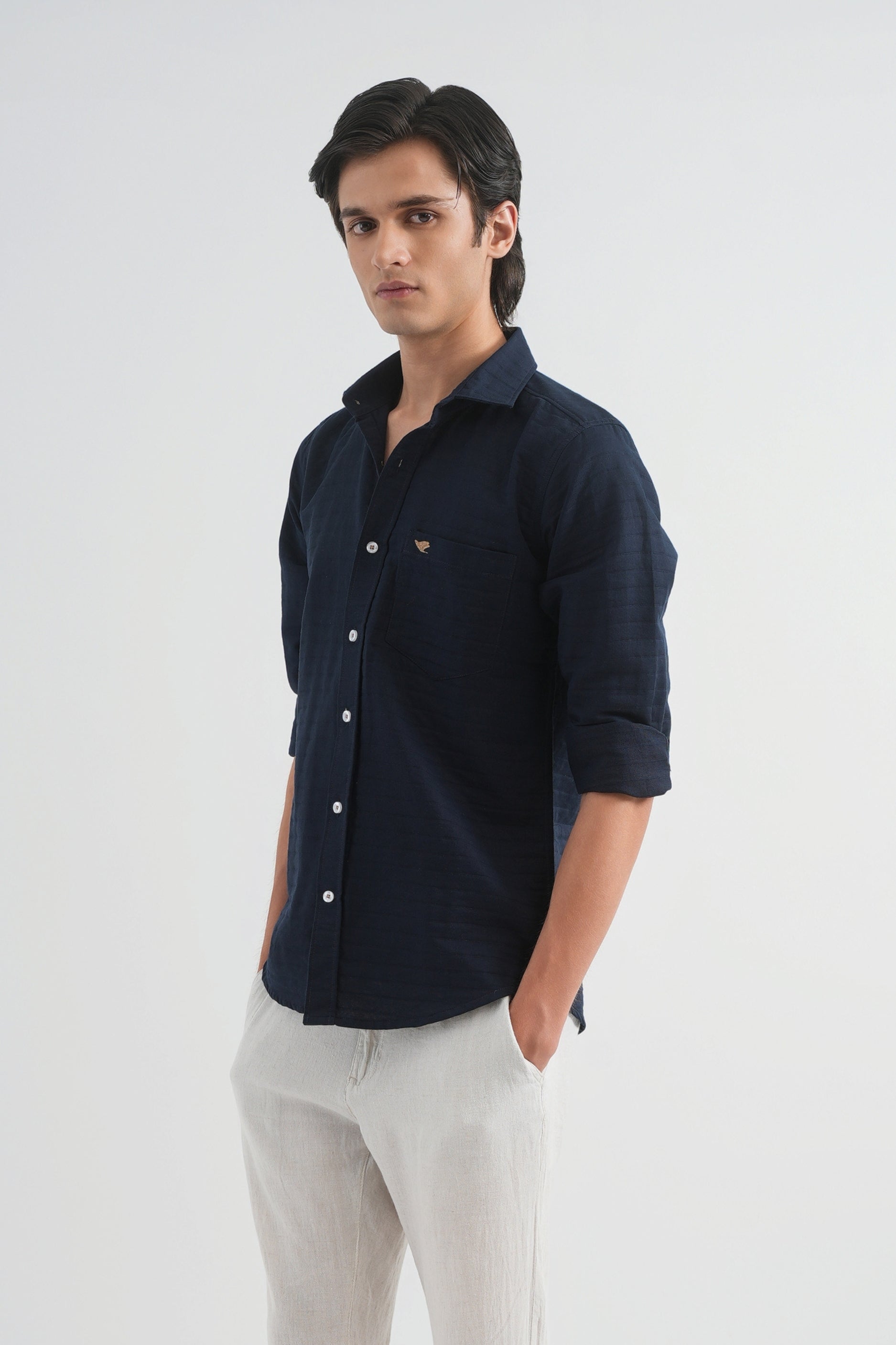 Man wearing a navy button-up shirt and light gray pants on a white background