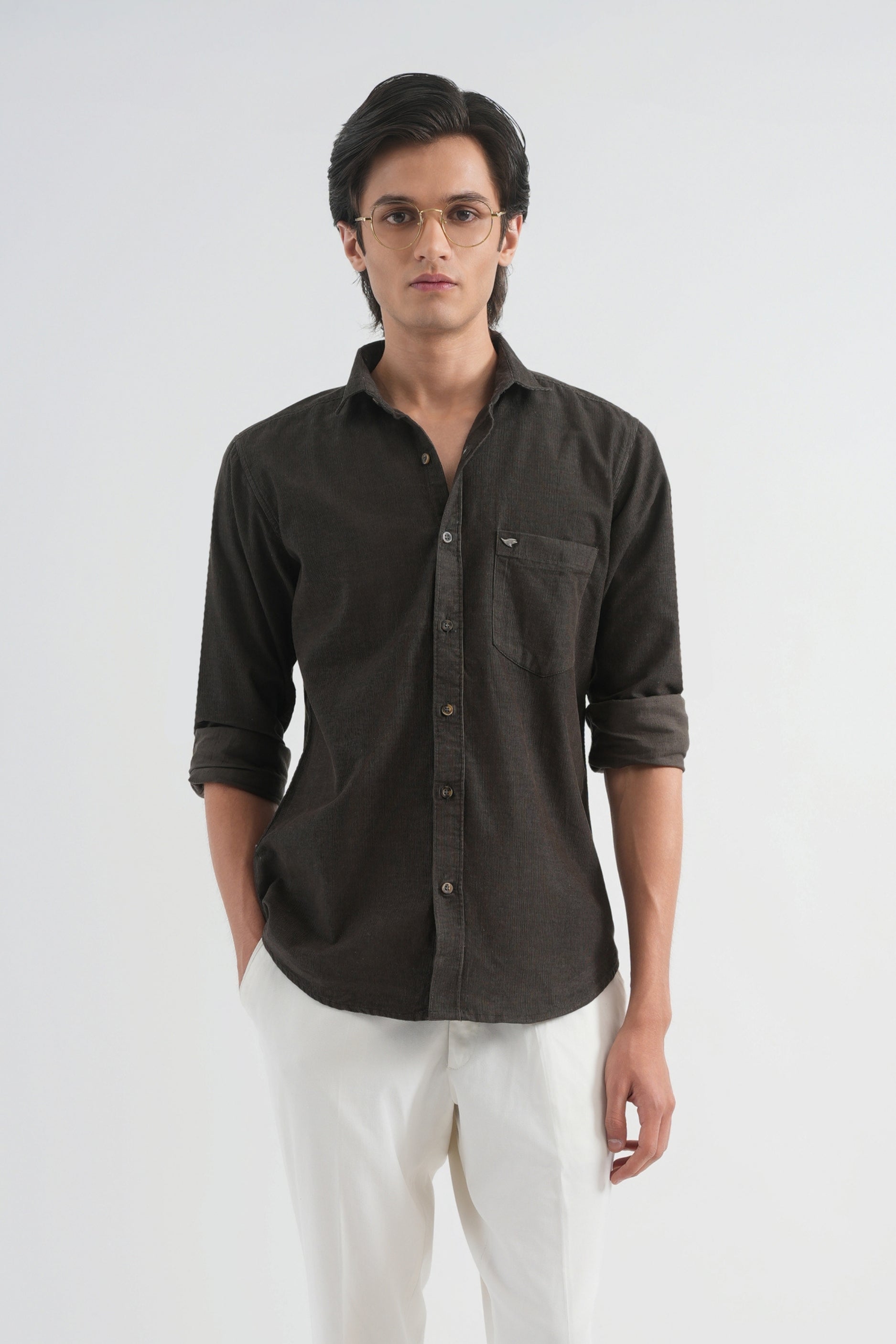 Man wearing a dark brown button-up shirt, white pants, and beige shoes on a white background