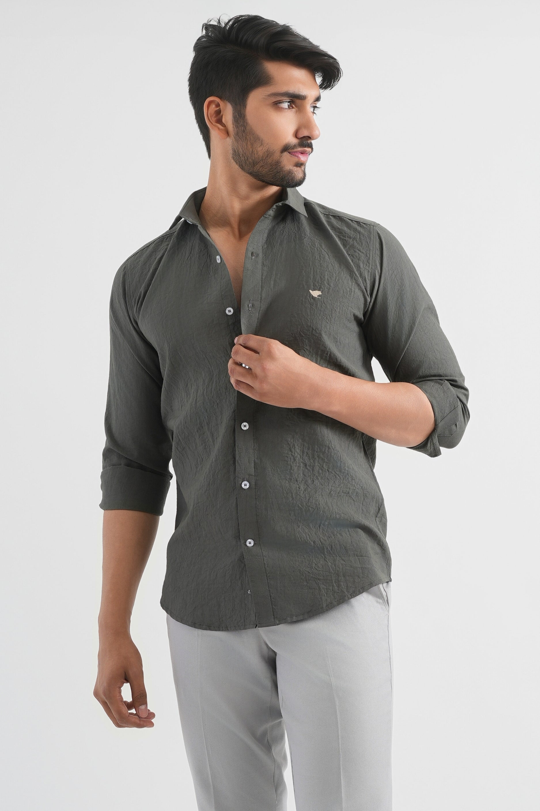 A man wearing a long-sleeved, button-up Lunar Green crushed cotton shirt with a collar, paired with light-colored trousers.