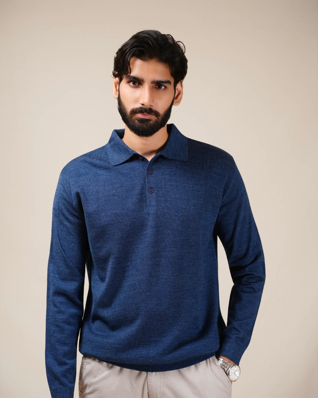 Man wearing a blue long-sleeve polo shirt against a beige background