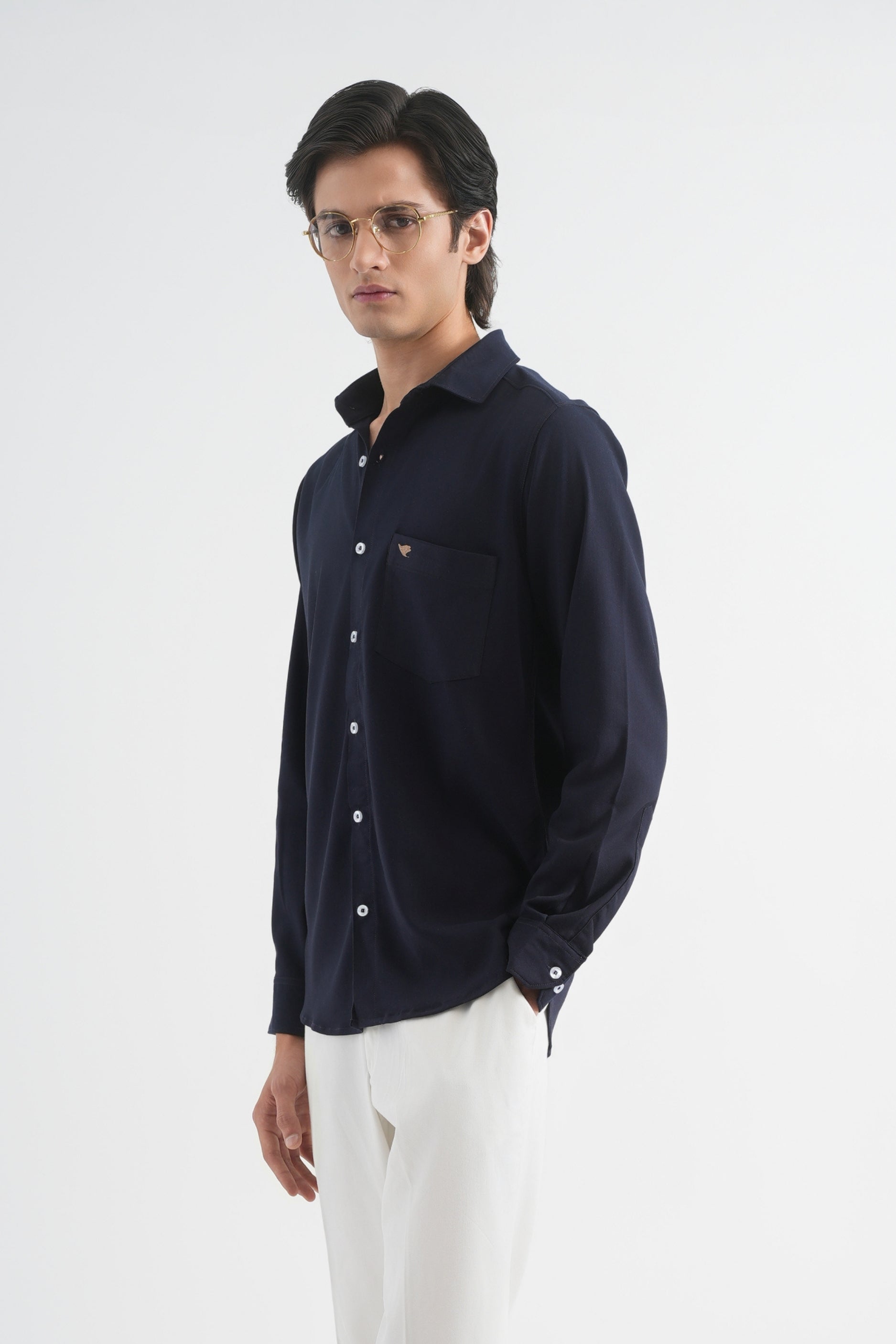 Man wearing a navy shirt, white pants, and dark shoes on a white background
