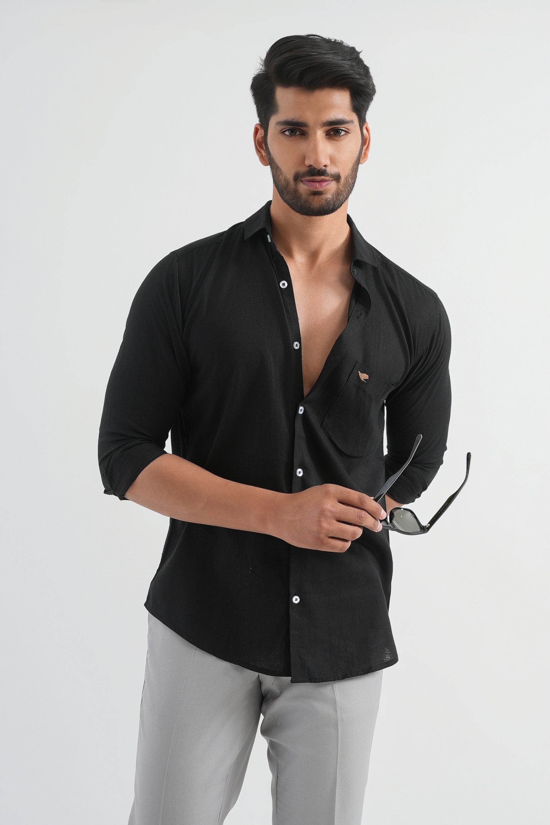 A man wearing a black Viscose Linen Shirt with buttons, collar visible, and holding sunglasses