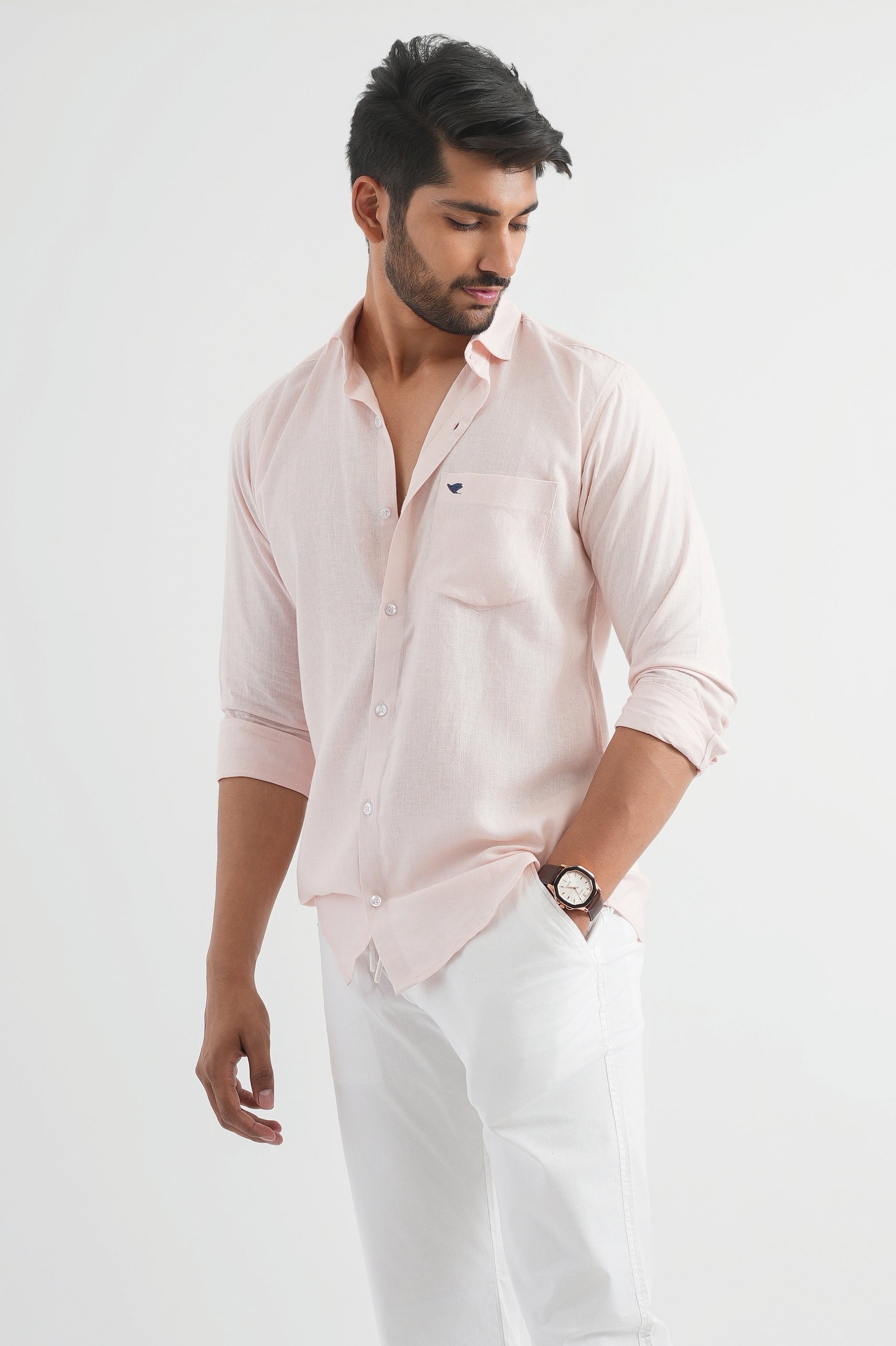 A man wearing an oyster pink linen shirt with white trousers.