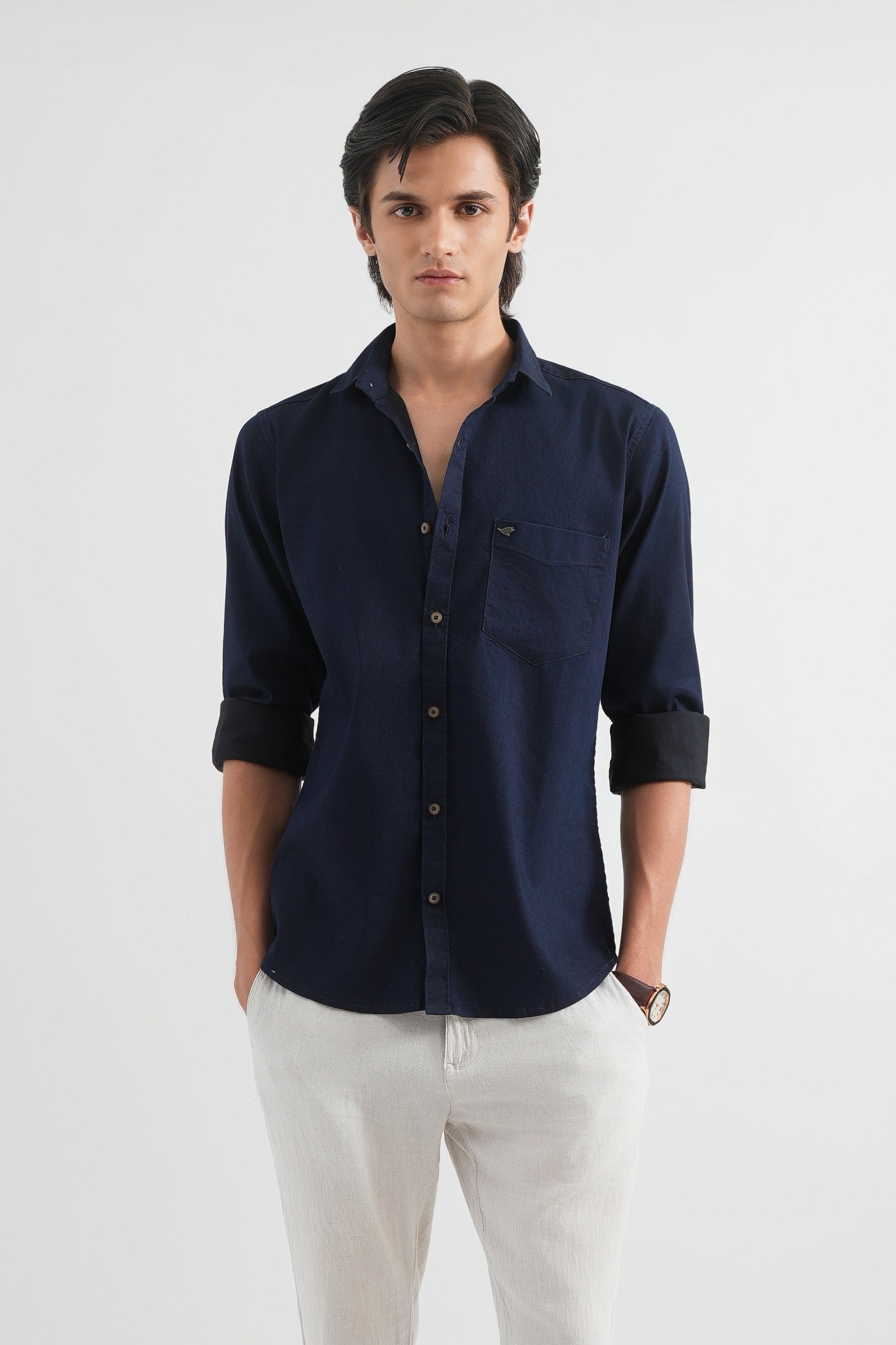 Man wearing a navy blue shirt and white pants on a white background