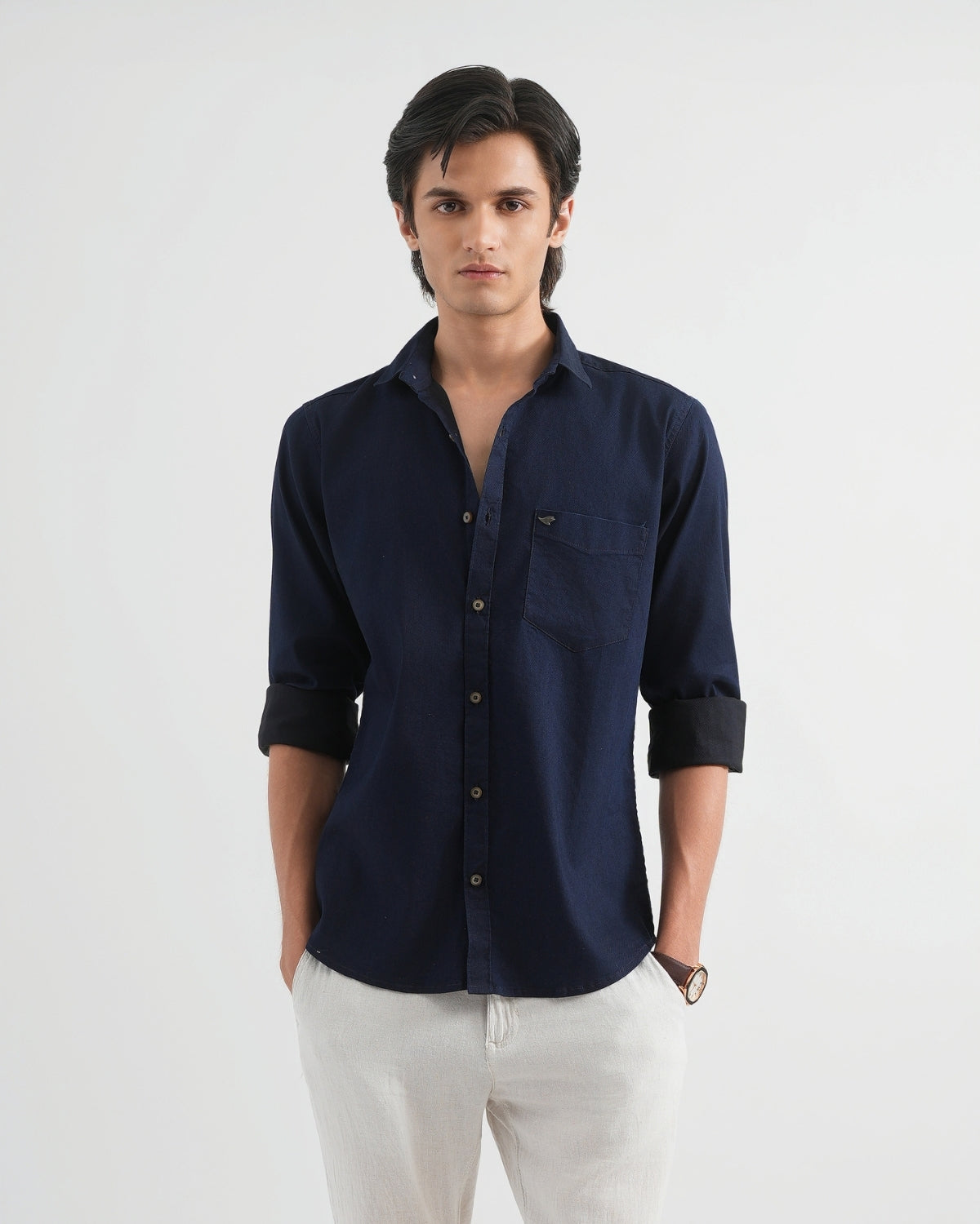 Man wearing a navy blue shirt with rolled-up sleeves on a white background