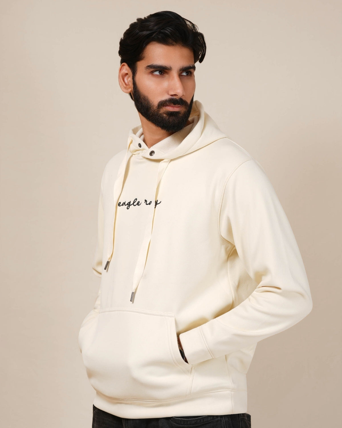 Man wearing a cream hoodie with a brand logo on a beige background