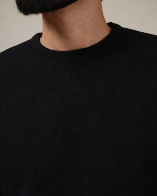 Close-up of a person wearing a black sweater against a neutral background