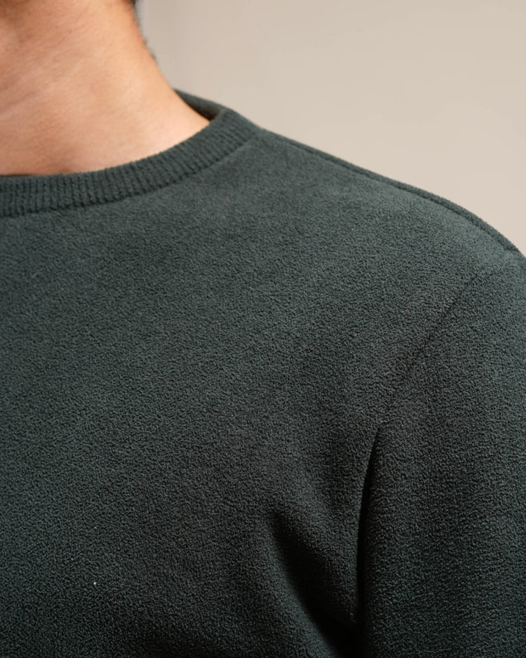 Close-up of a person wearing a dark green sweater against a neutral background