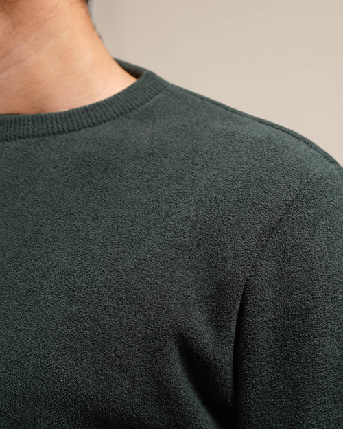Close-up of a person wearing a dark green sweater against a neutral background