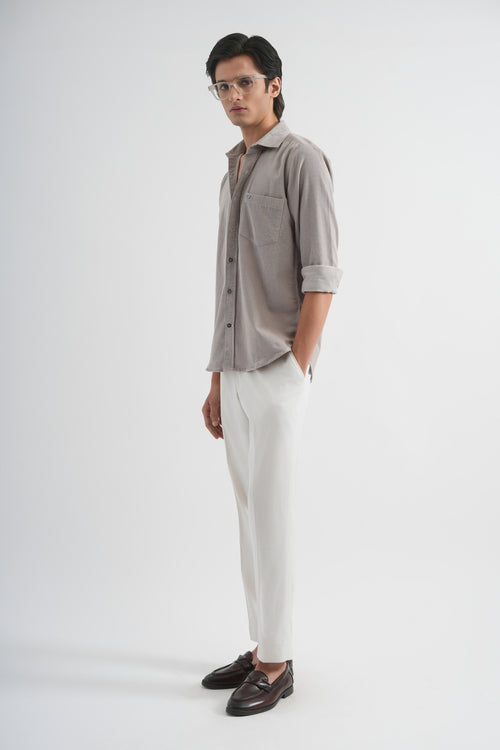 Man wearing a light gray button-up shirt and white pants on a plain background