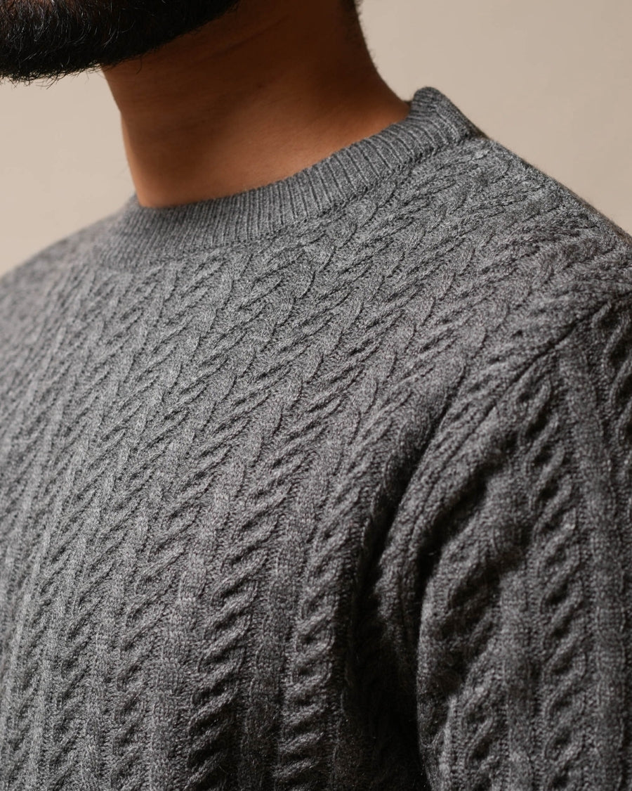 Close-up of a person wearing a gray cable knit sweater against a beige background