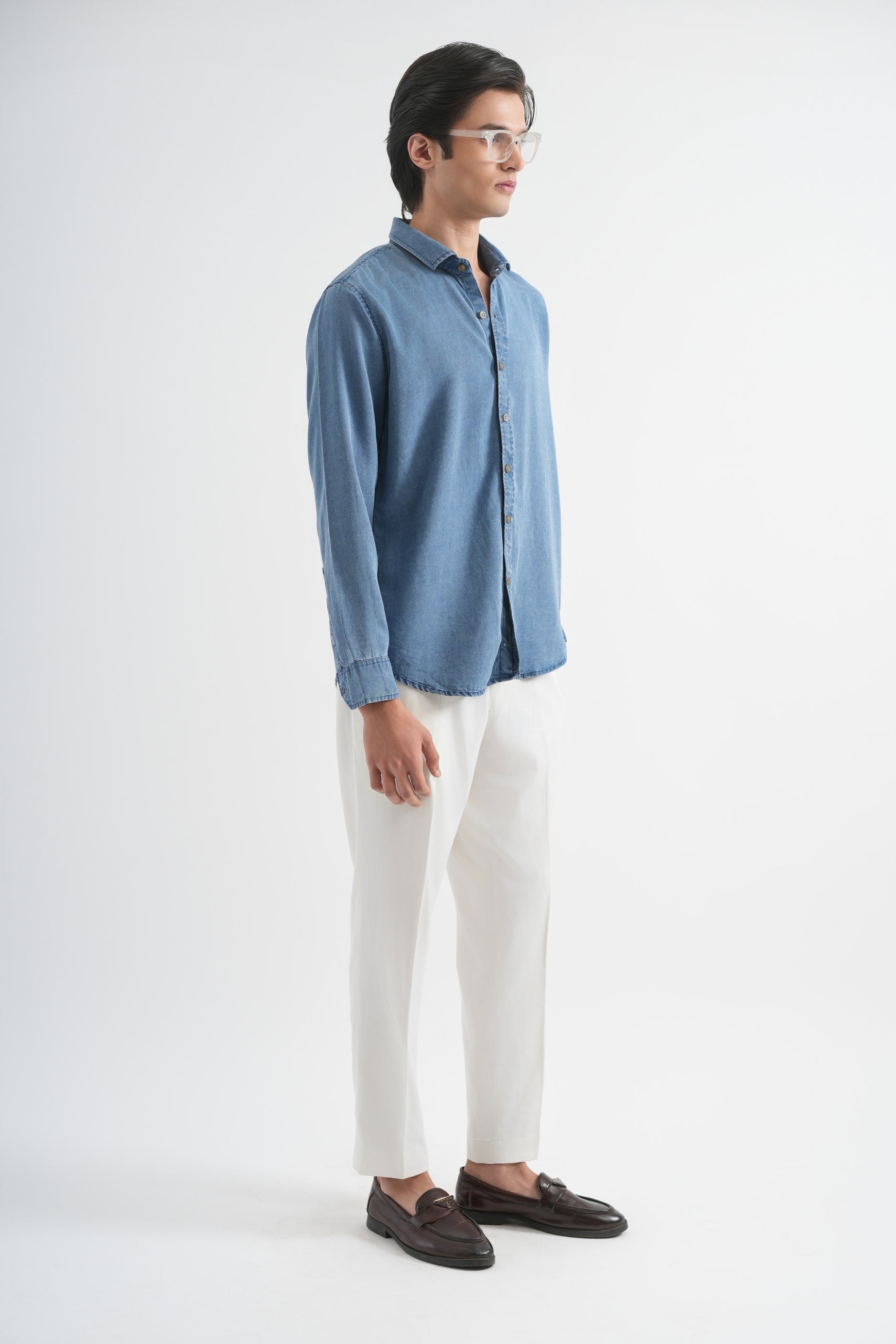 Man wearing a blue denim shirt and white pants on a white background