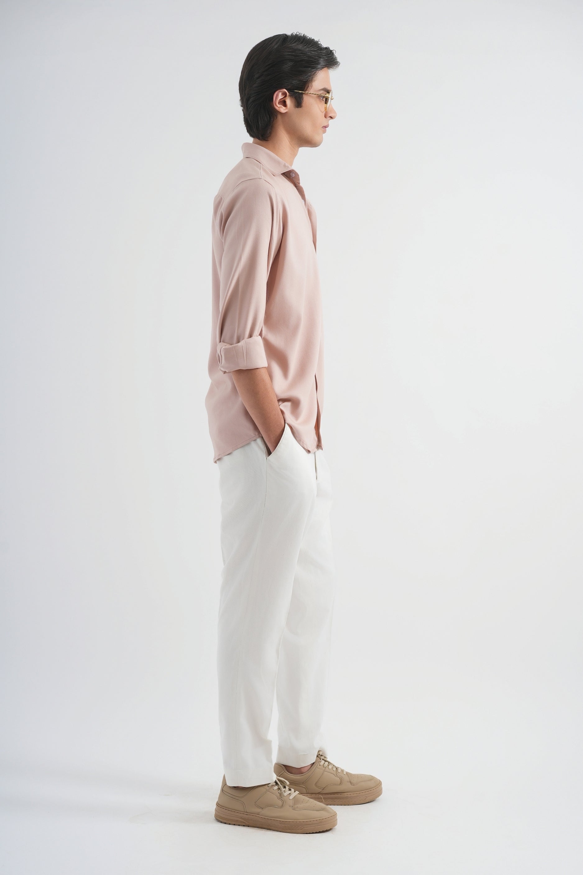 Person wearing a light pink shirt, white pants, and brown shoes on a white background