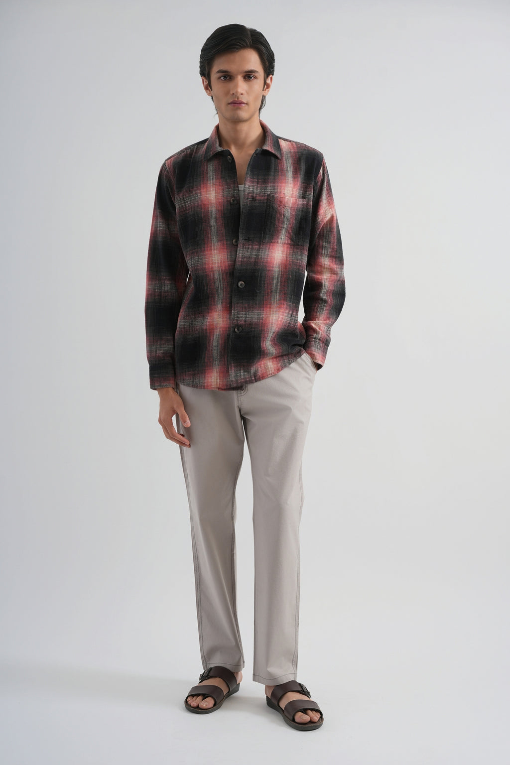 Man wearing a plaid shirt and light gray pants on a white background