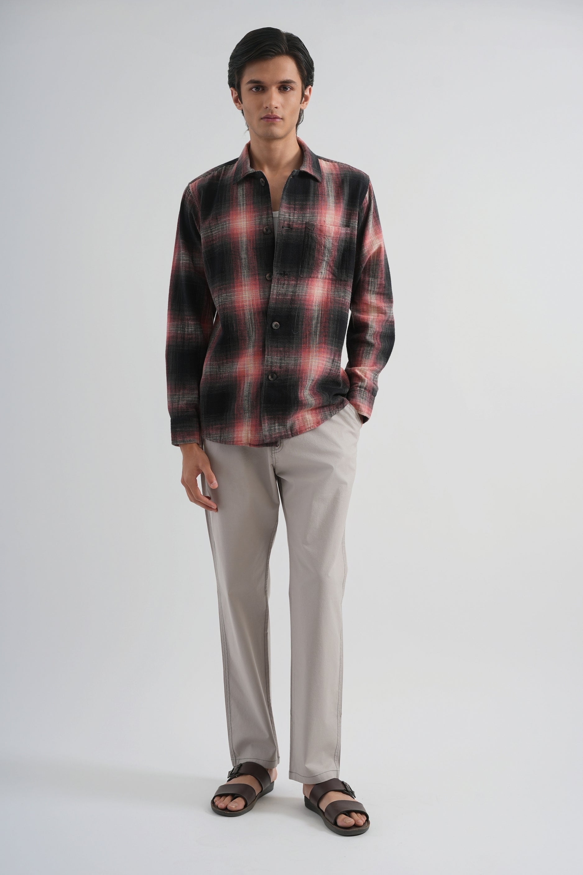 Man wearing a plaid shirt and light gray pants on a white background
