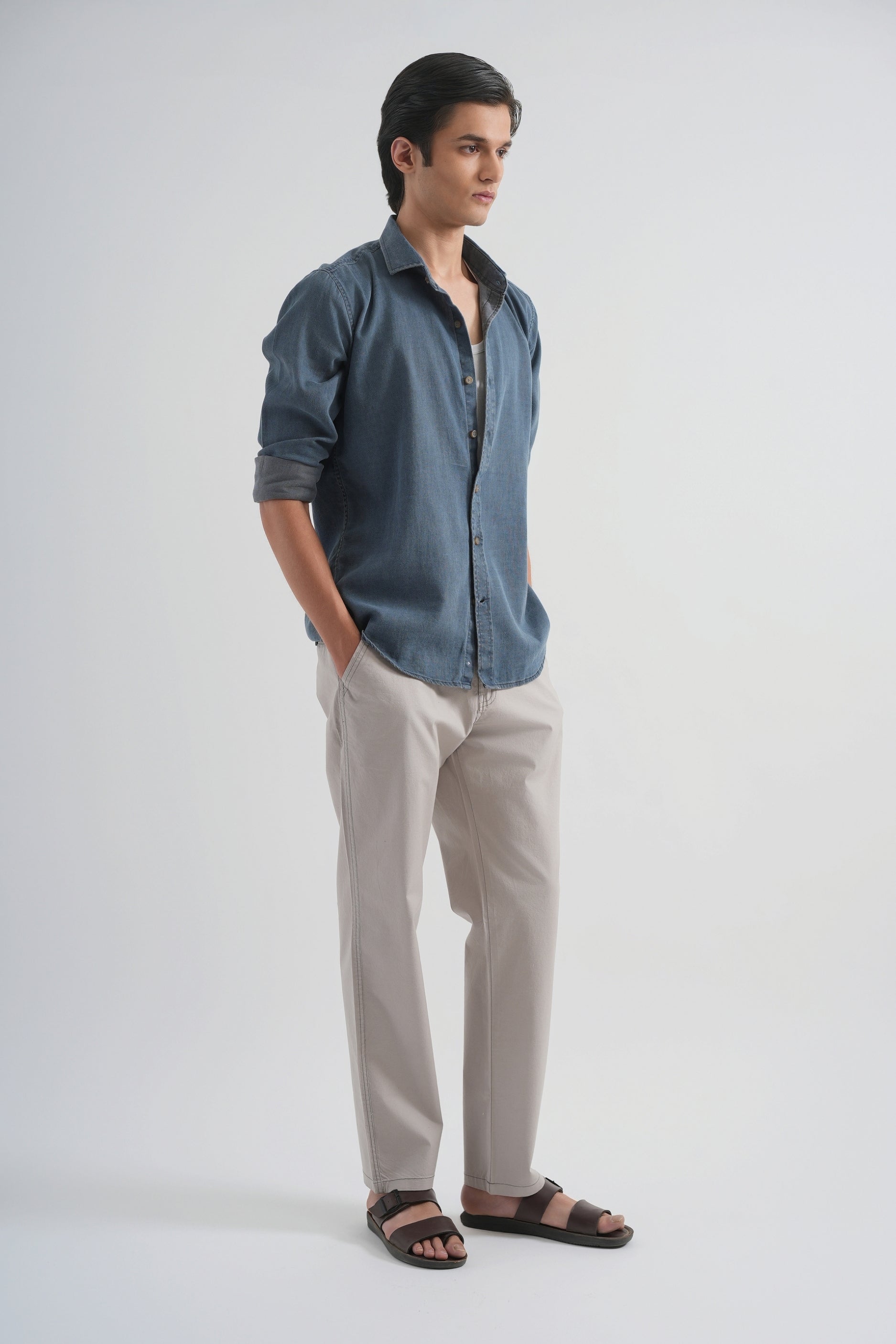 Man wearing a blue shirt and beige pants on a white background