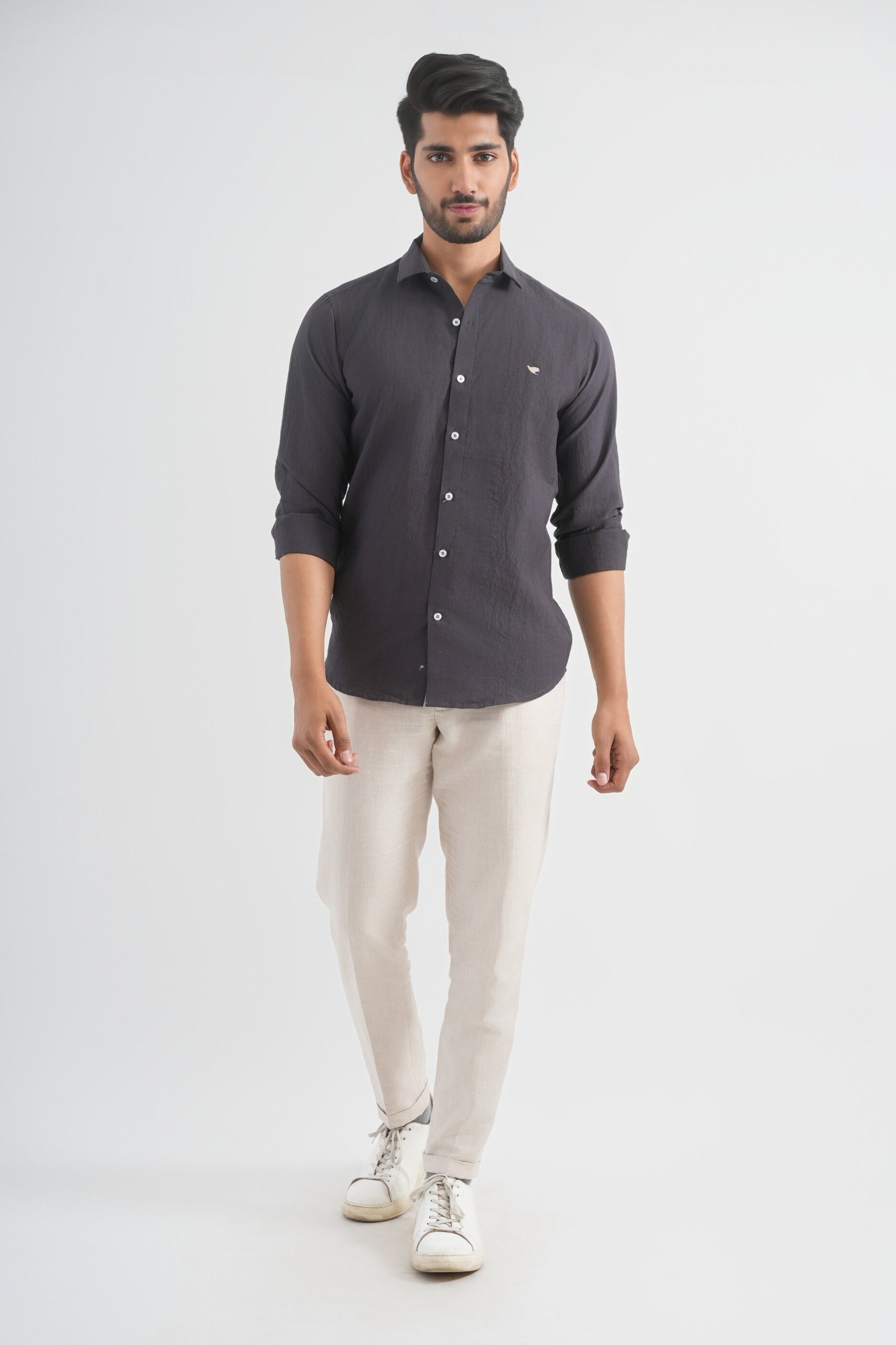 Man wearing a dark gray button-up shirt and beige pants on a white background
