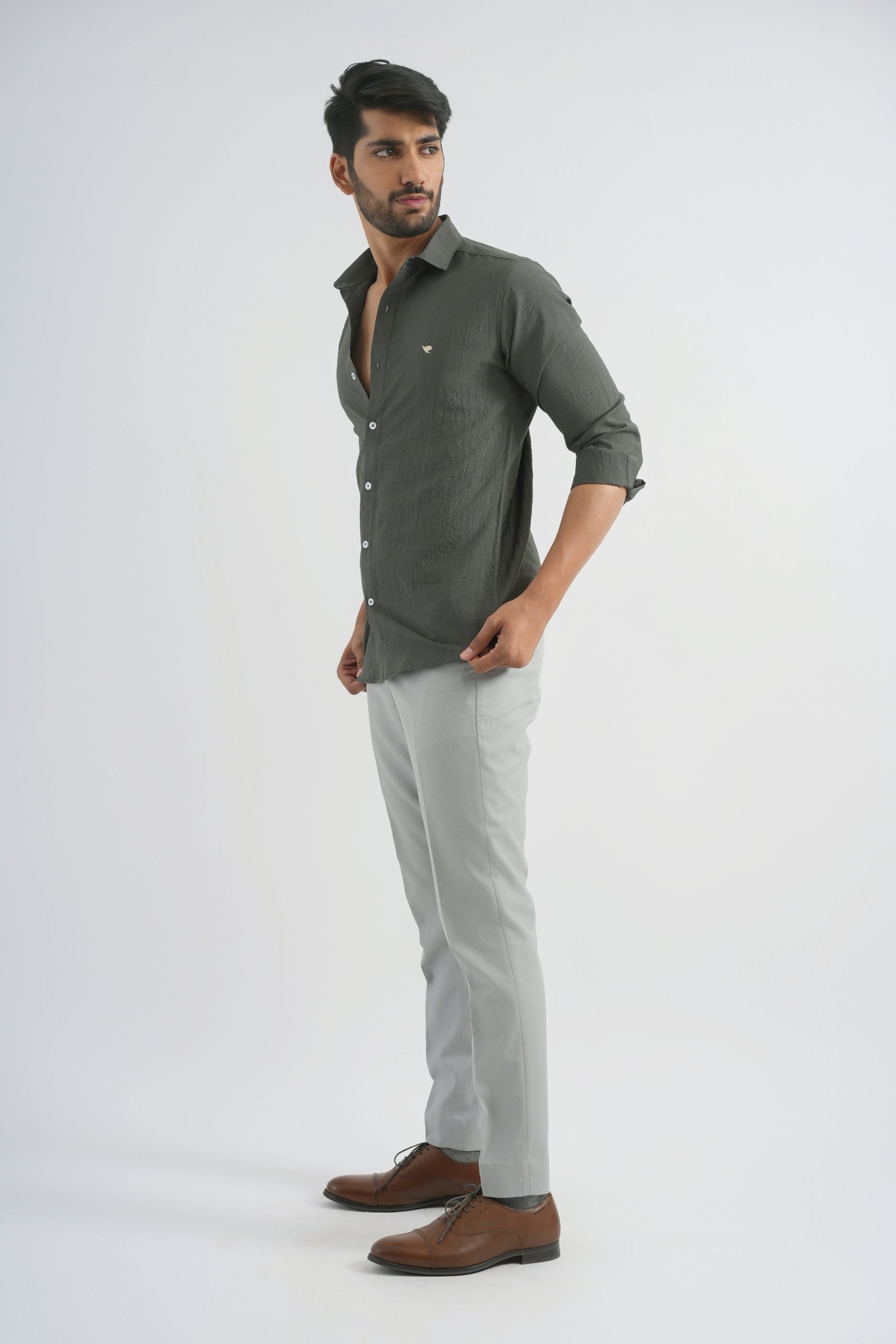 Man wearing a green shirt, light gray pants, and brown shoes on a white background