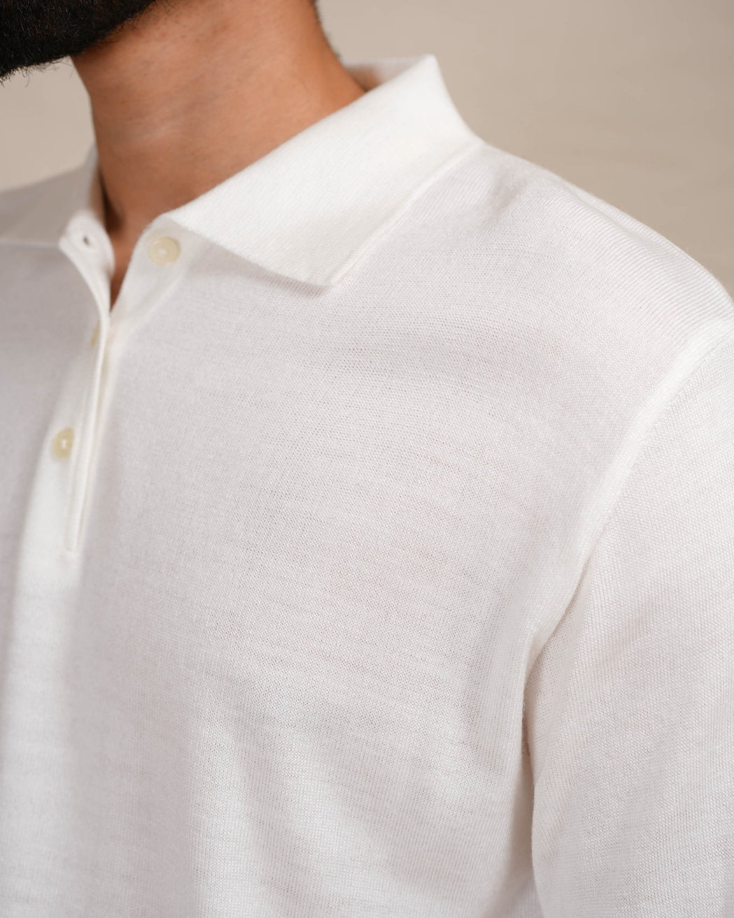 Man wearing a white long-sleeve polo shirt against a beige background