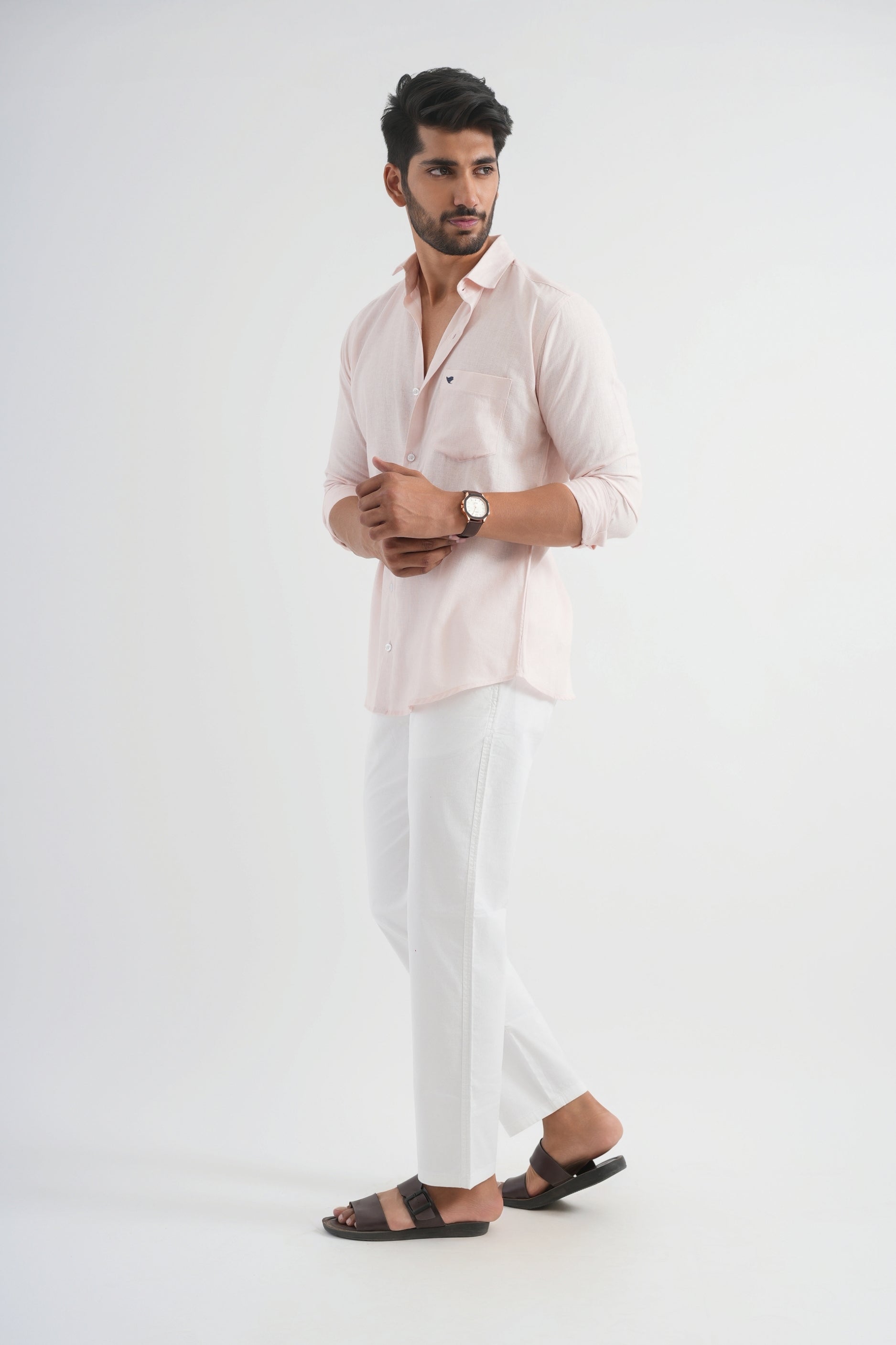 Man wearing a light pink linen shirt and white pants on a white background