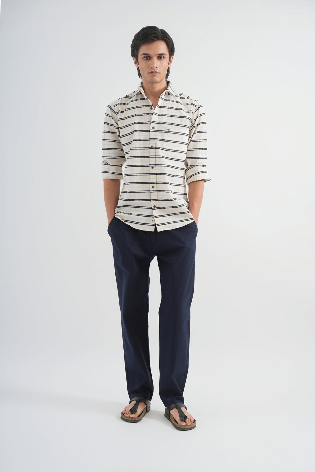 Man wearing a striped shirt and dark pants on a white background