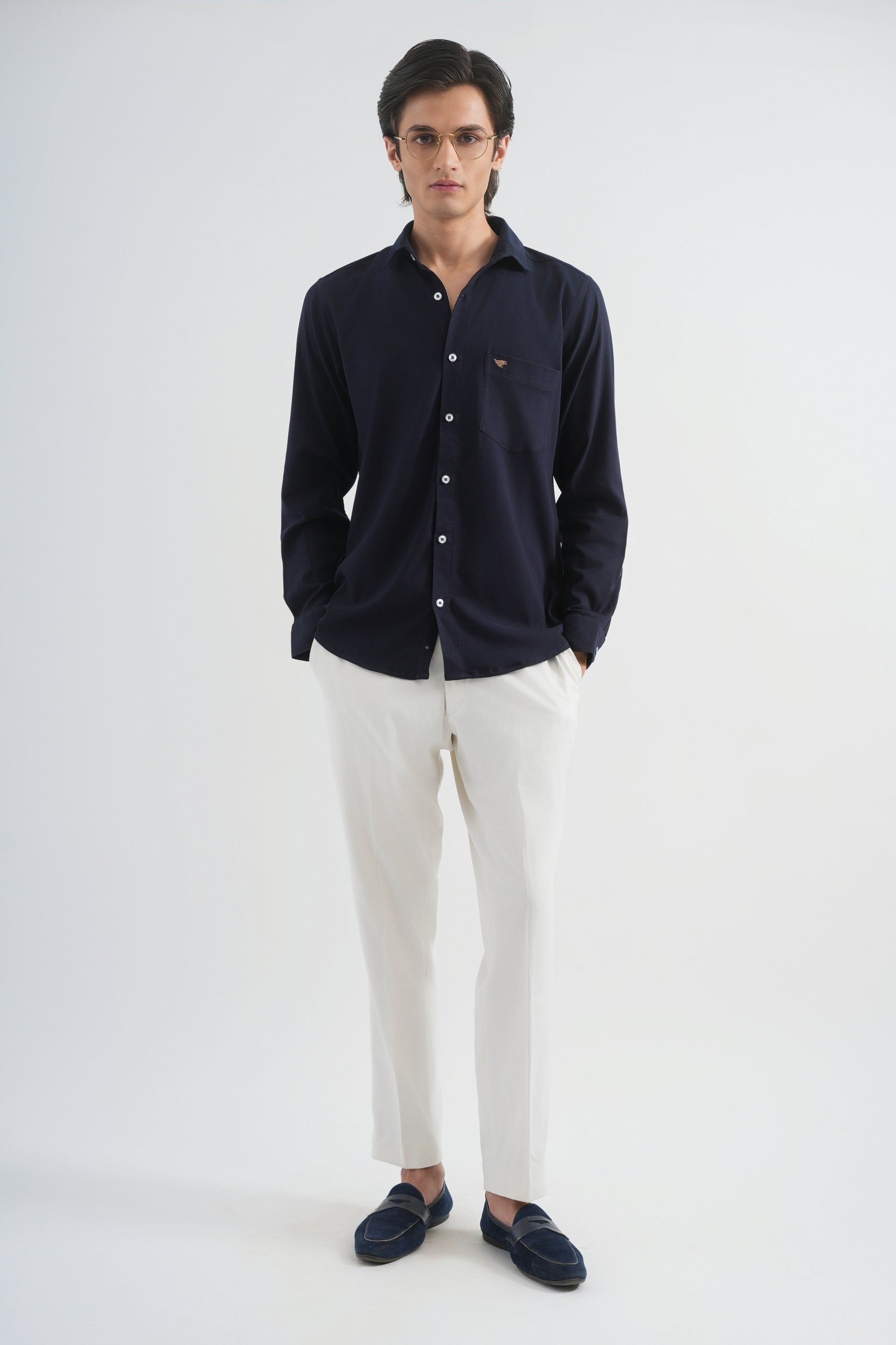 Man wearing a navy button-up shirt and white pants on a white background