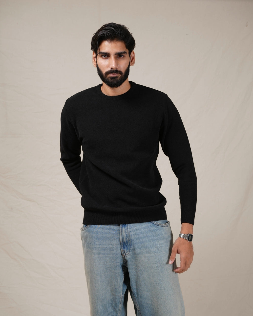 Man wearing a black sweater and light blue jeans against a plain background