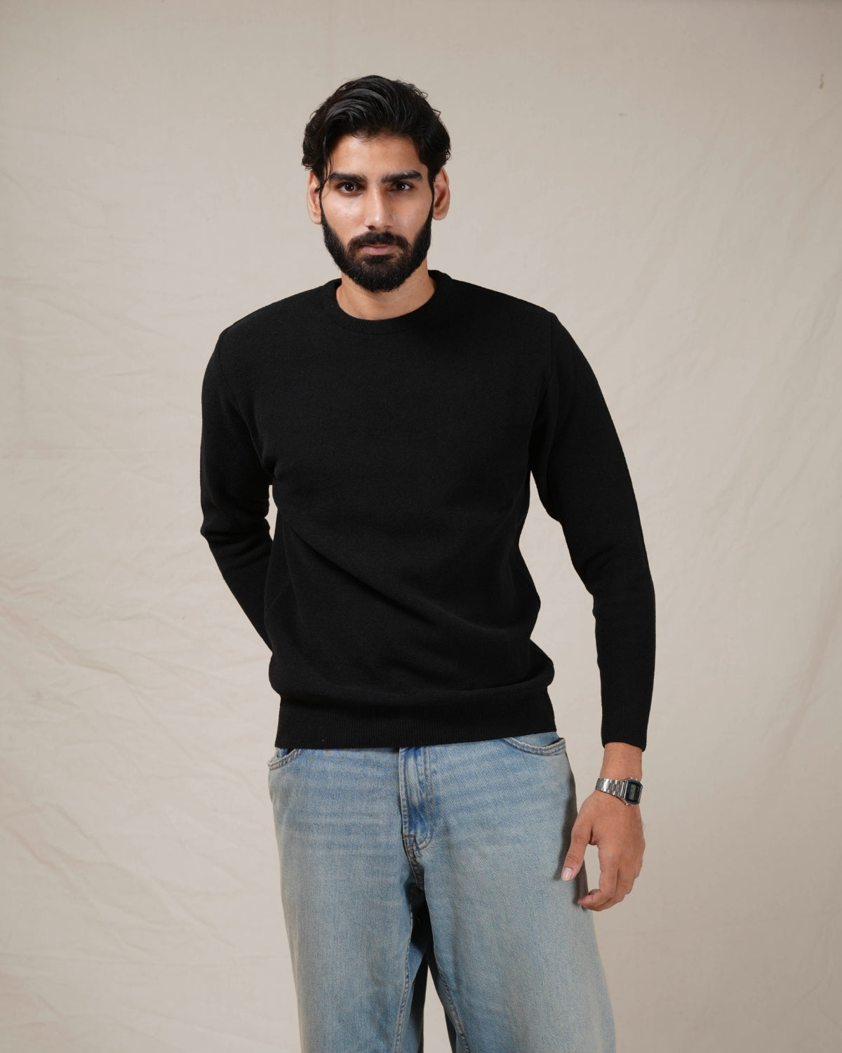 Man wearing a black sweater and light blue jeans against a plain background