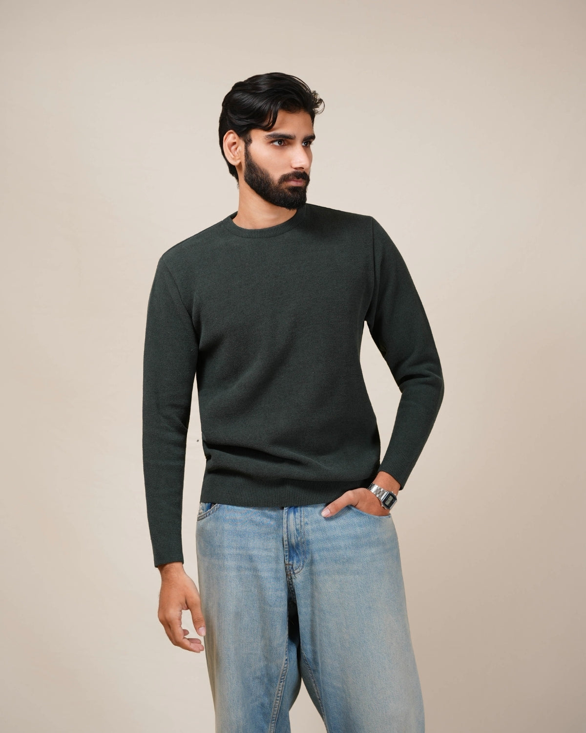 Man wearing a dark green sweater and light blue jeans against a beige background