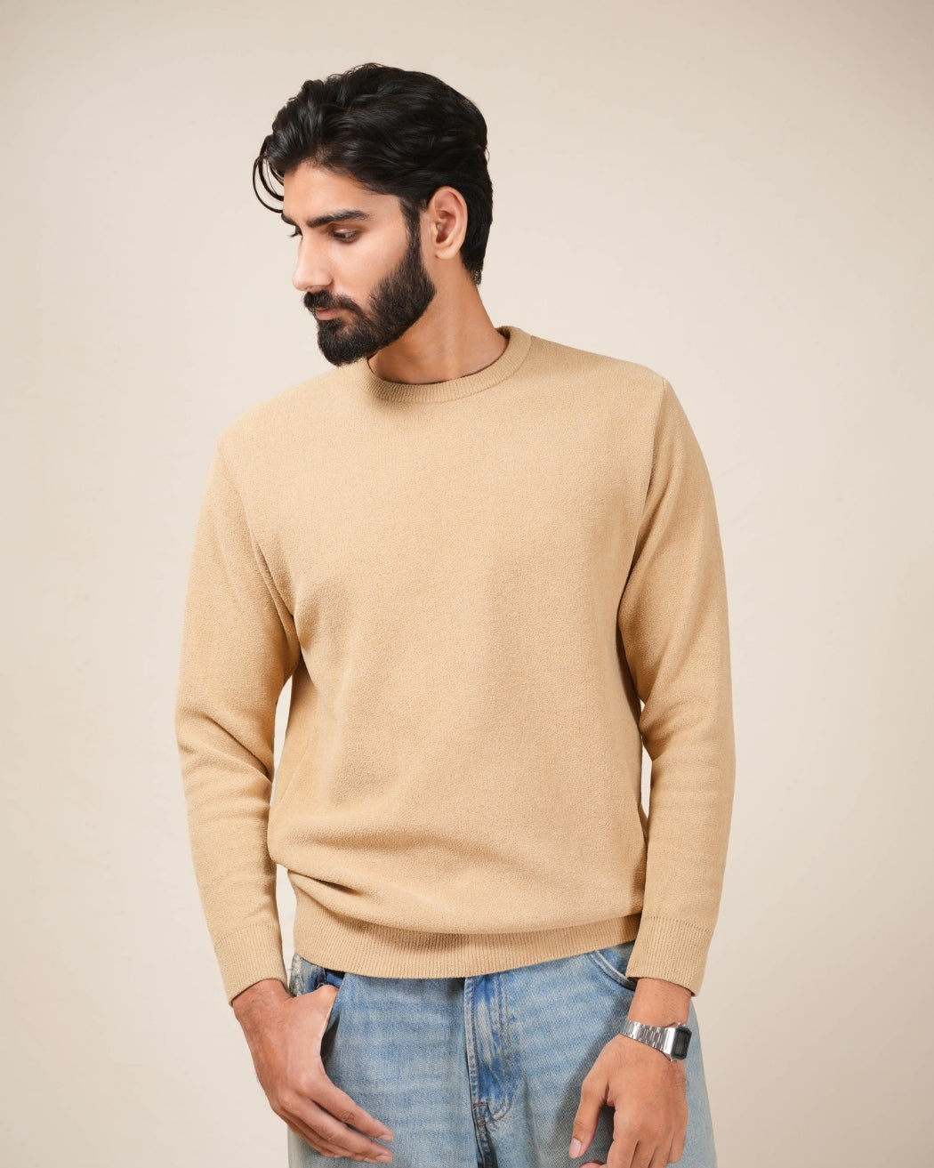Man wearing a beige sweater and blue jeans against a beige background