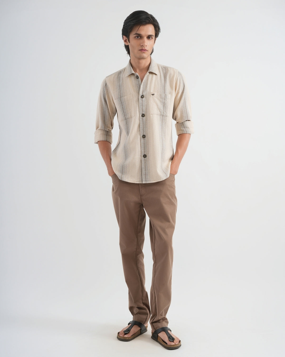 Man wearing a beige button-up shirt and brown pants on a white background