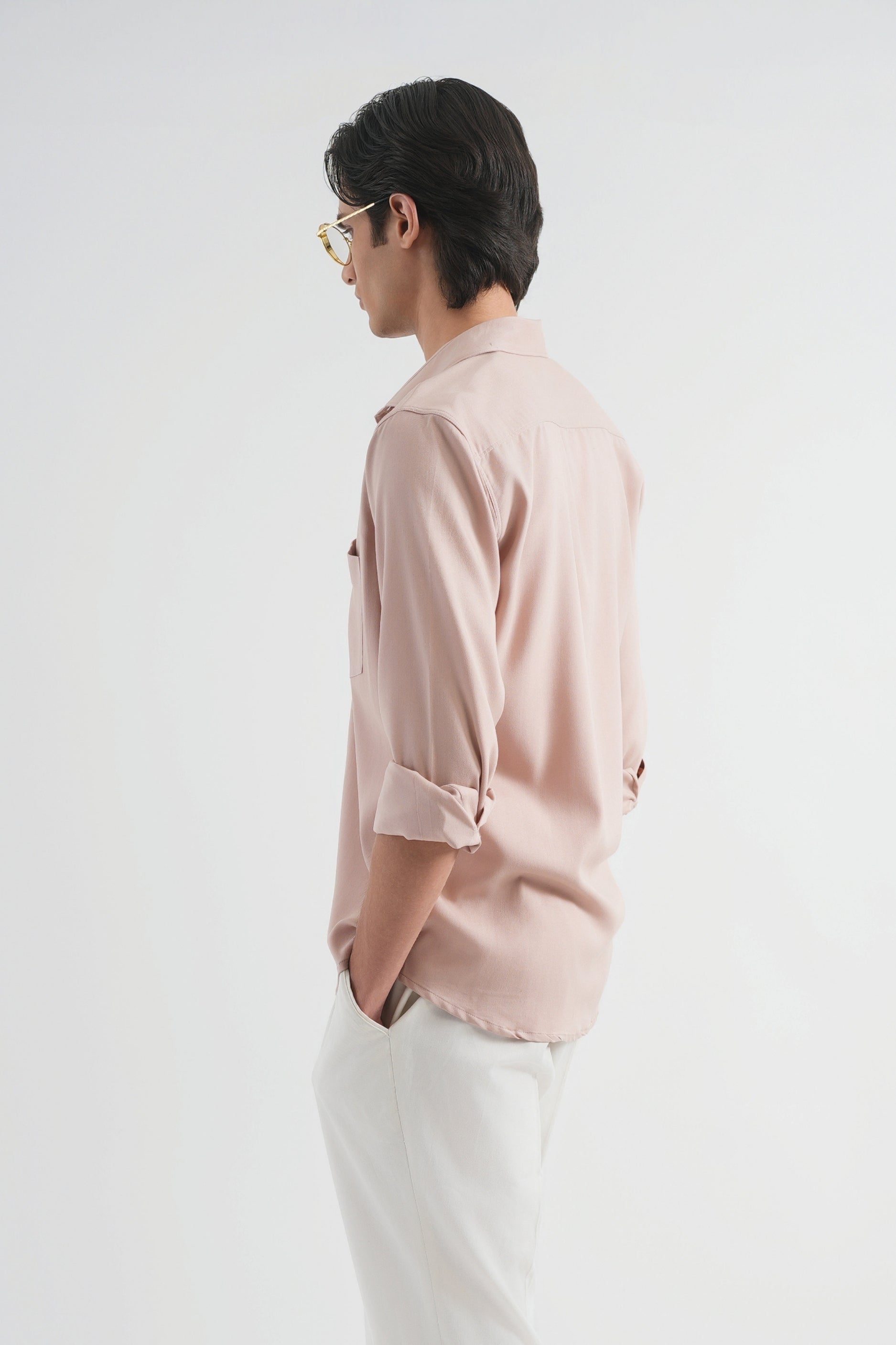 Person wearing a light pink shirt, white pants, and brown shoes on a white background