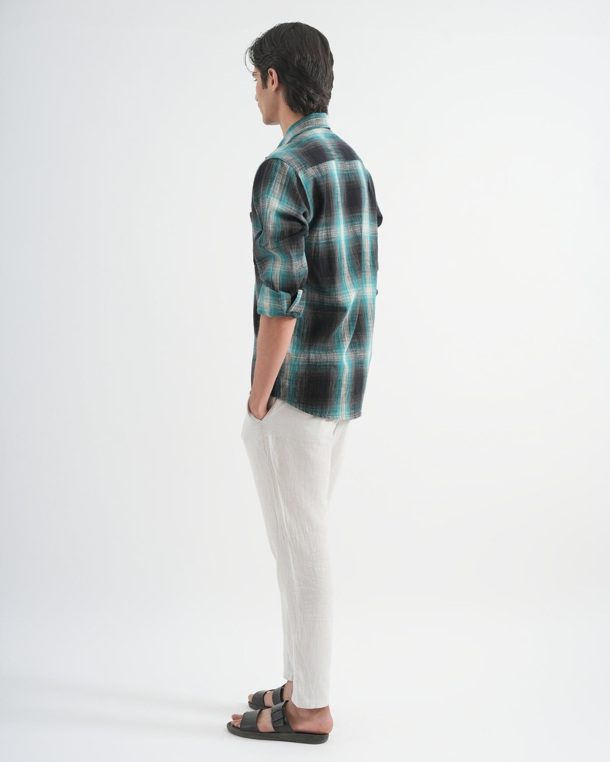 Person wearing a green and black plaid shirt with white pants on a white background