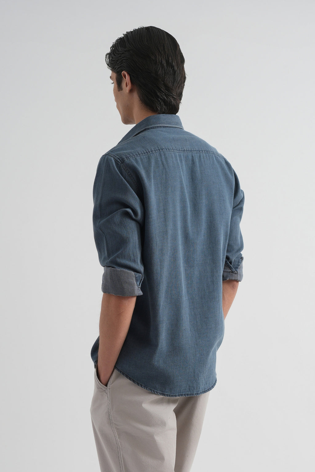 Person wearing a blue denim shirt and beige pants on a white background