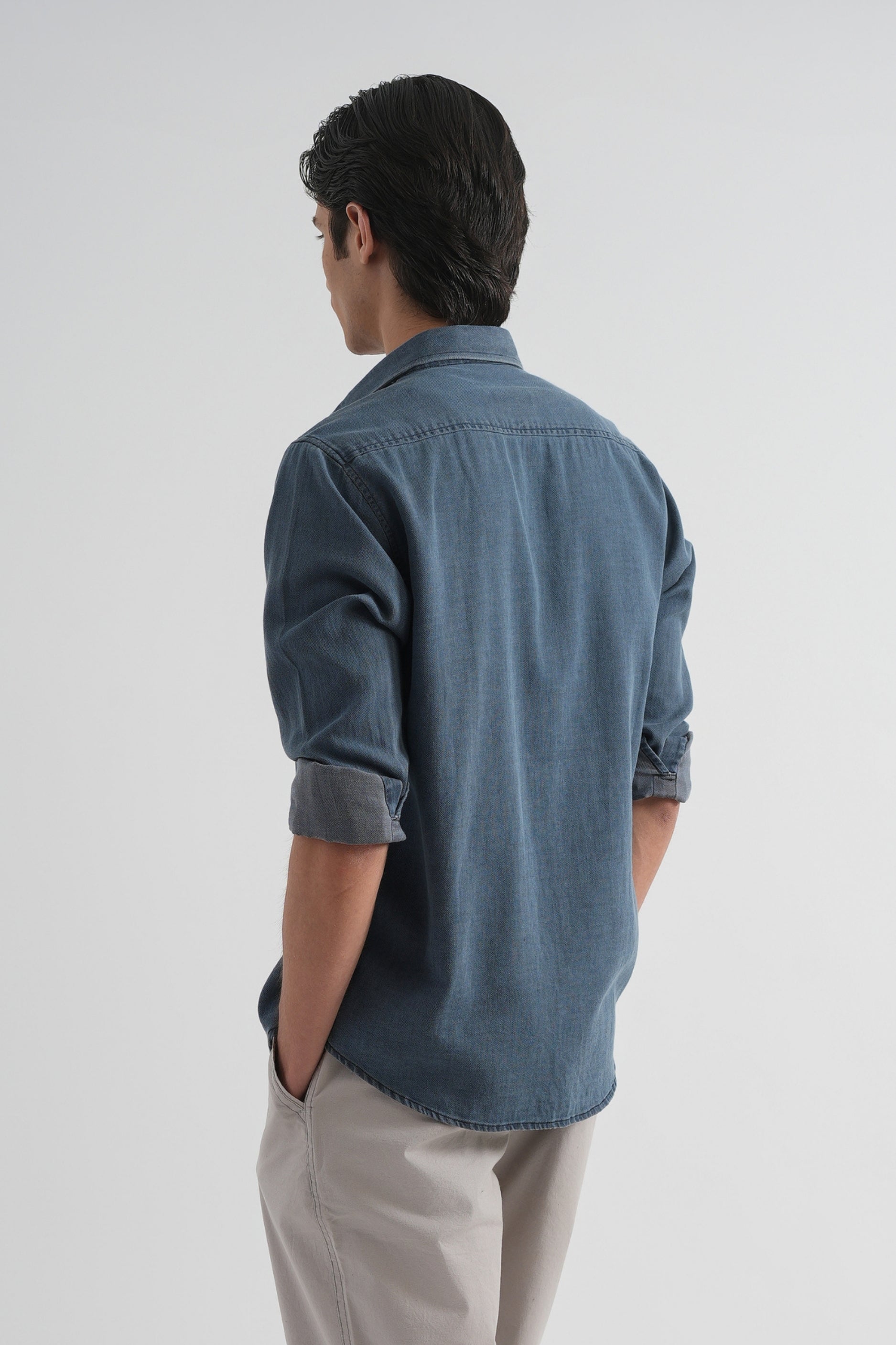 Person wearing a blue denim shirt and beige pants on a white background
