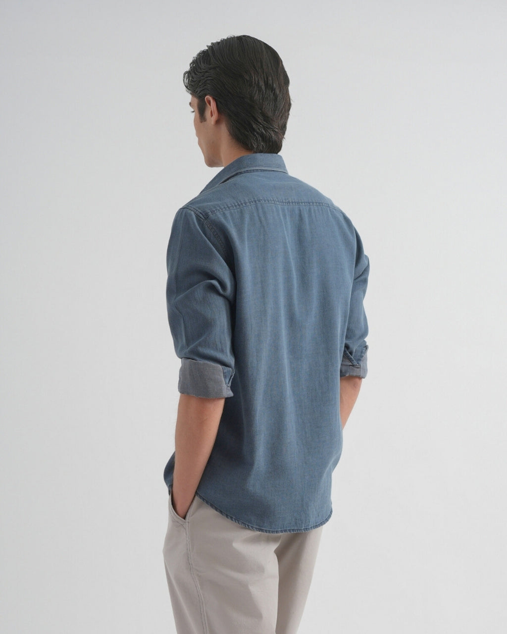 Person wearing a blue denim shirt and beige pants on a white background